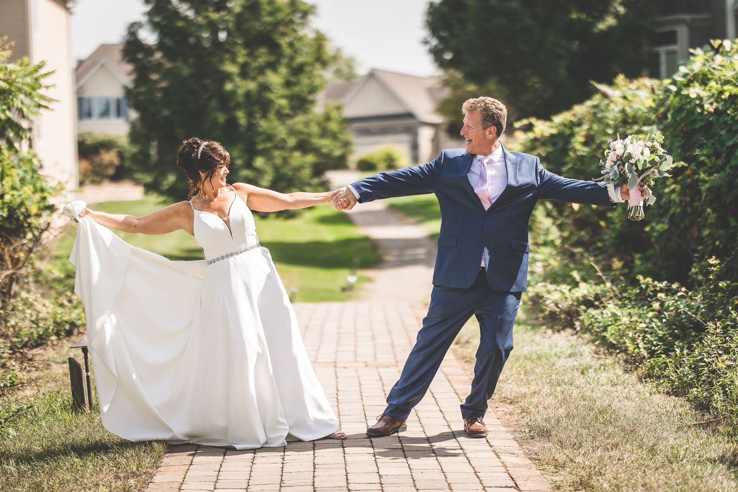 Couple poses for romantic wedding photos on a brick pathway surrounded by greenery.