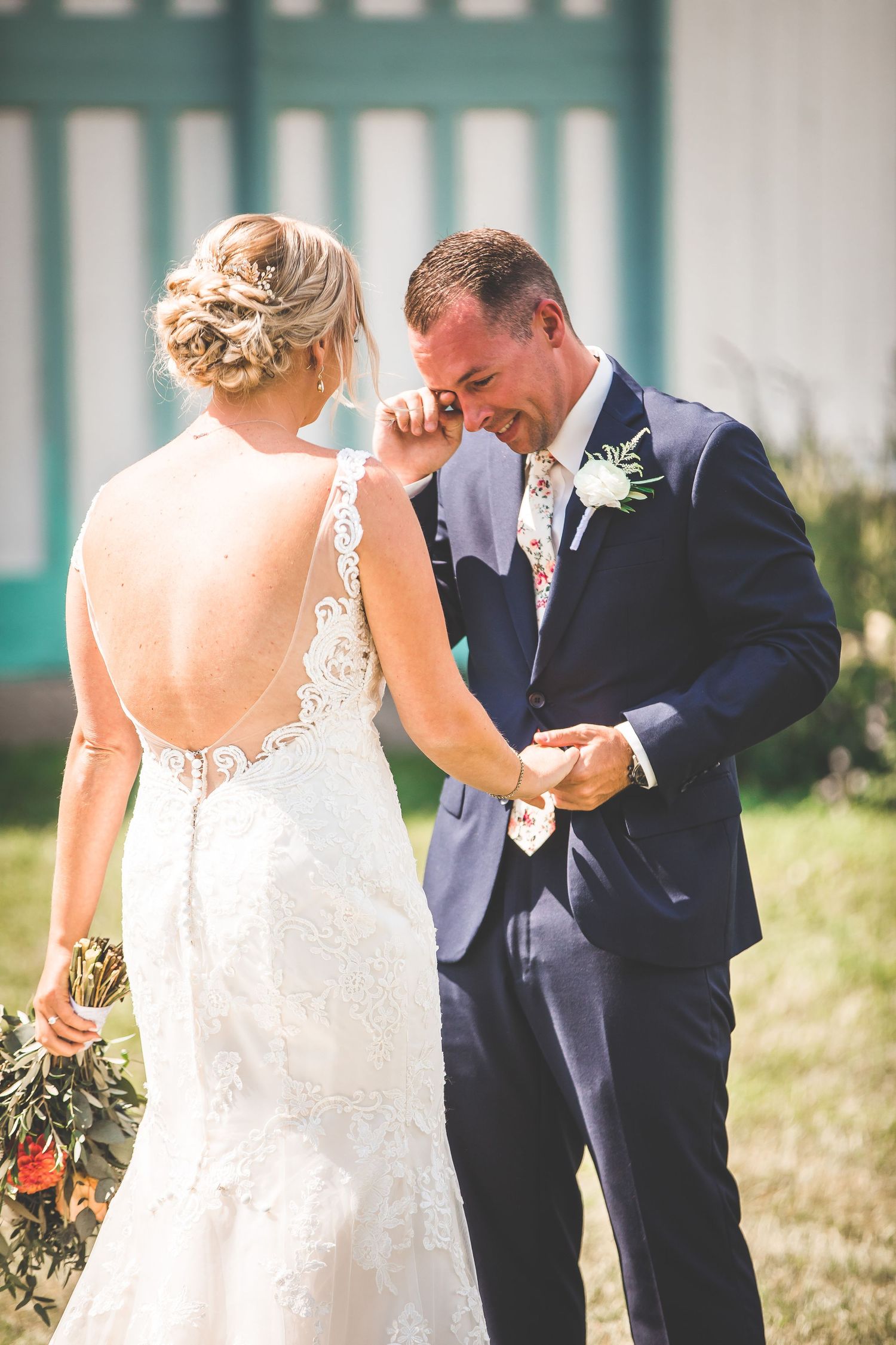 An emotional first look moment between a couple in front of a turquoise and white backdrop.