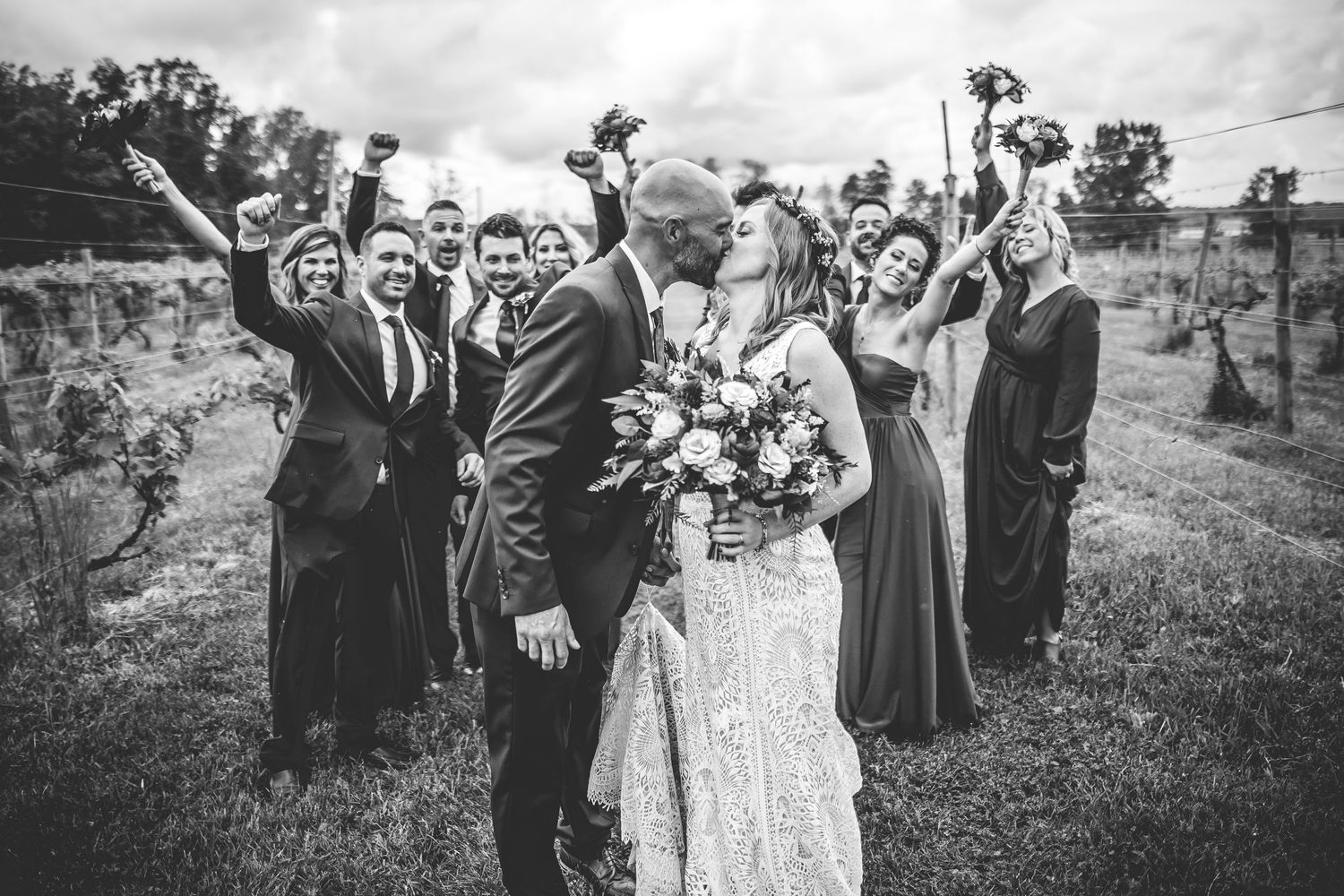 Black and white photo of wedding party celebrating in vineyard landscape.