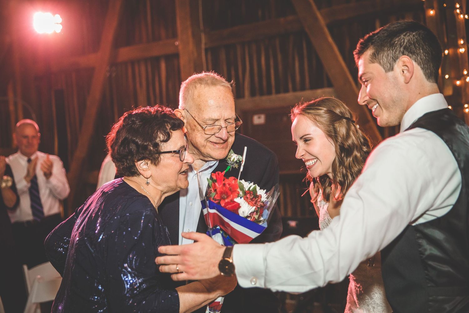 Wedding party celebrates on the dance floor under string lights at an indoor reception.