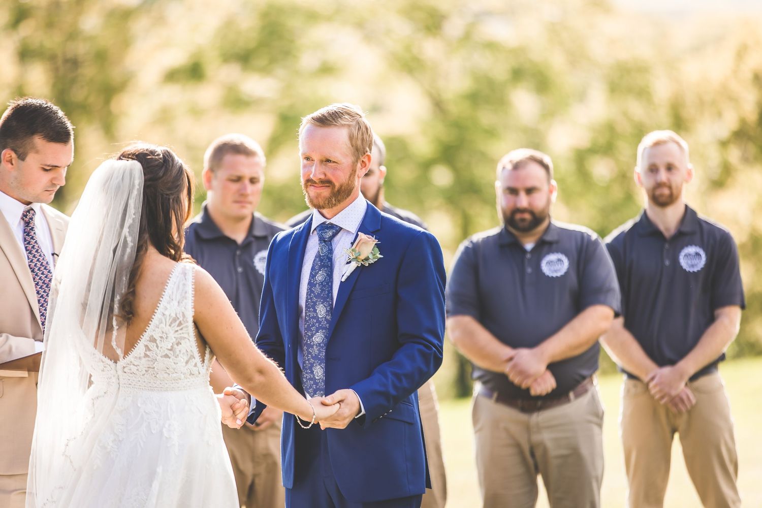 Intimate outdoor wedding ceremony with attendants standing in a semi-circle on a sunny afternoon.