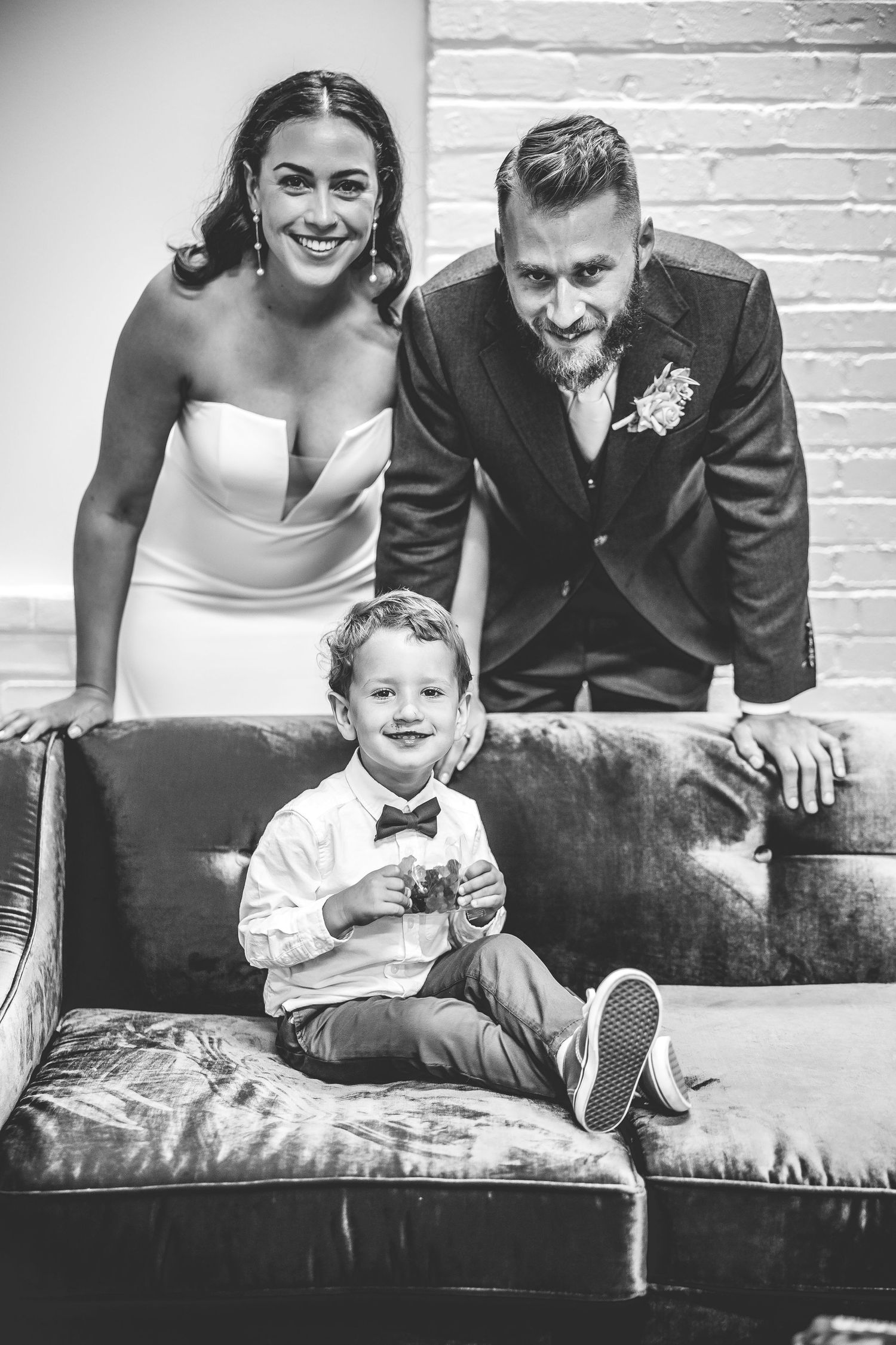 Family portrait session on a vintage leather couch against white brick wall.