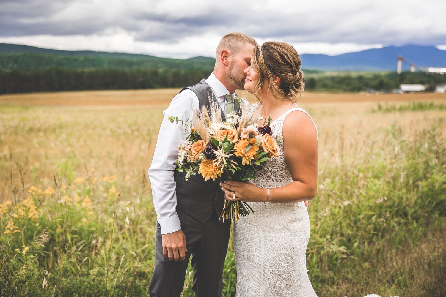 Couple sharing intimate moments in a rustic field with mountains in background.