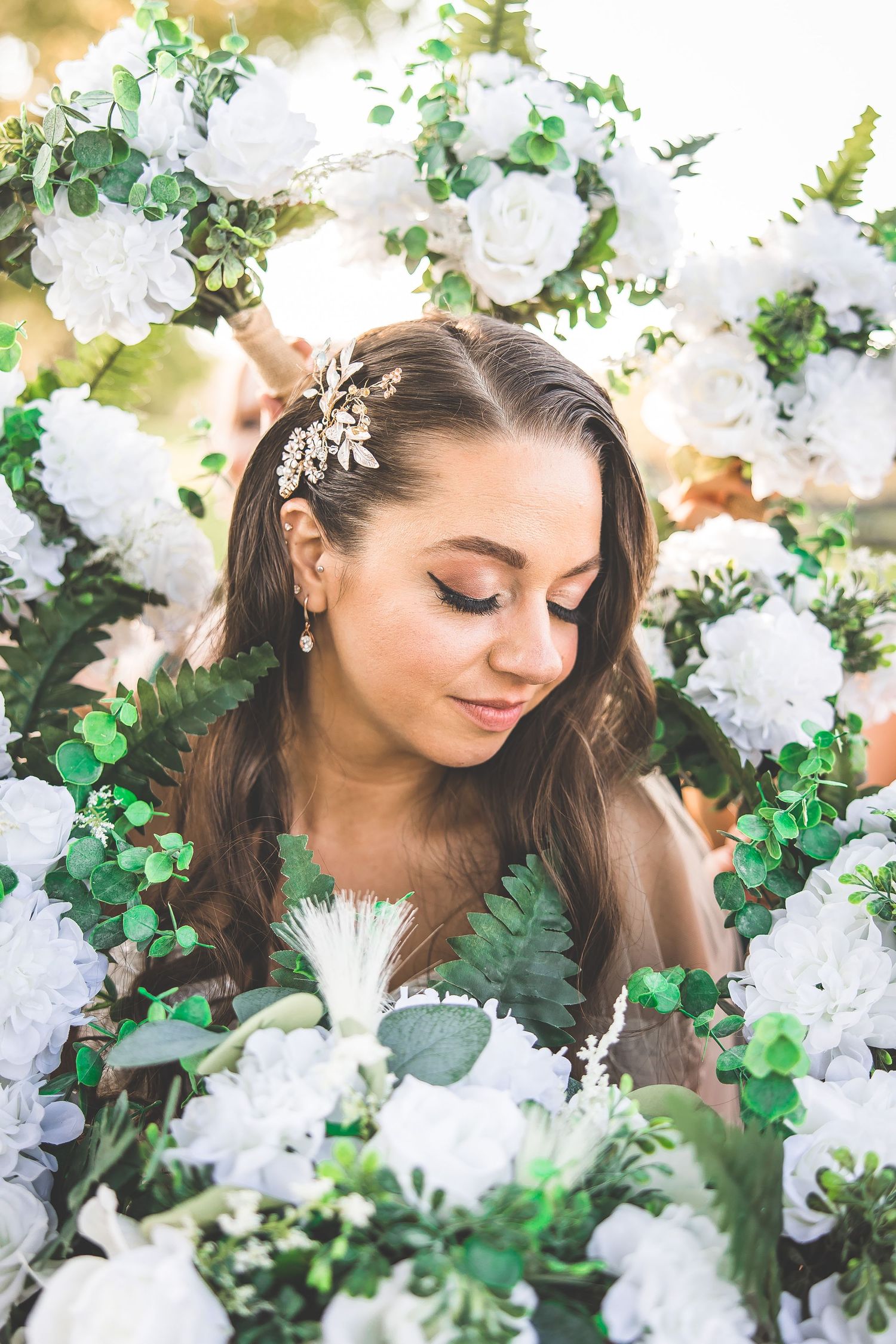 Romantic bridal portraits surrounded by white roses and greenery in natural light.