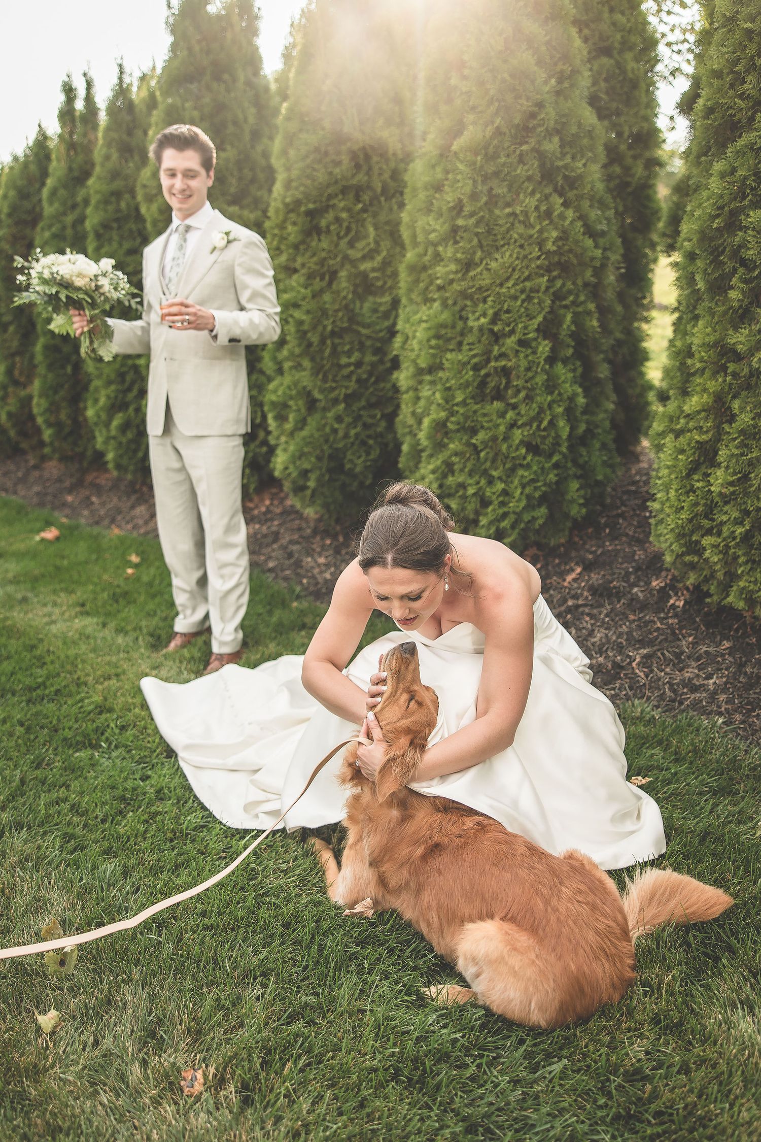 Sweet moment between a bride in white dress and golden retriever dog on grassy lawn.