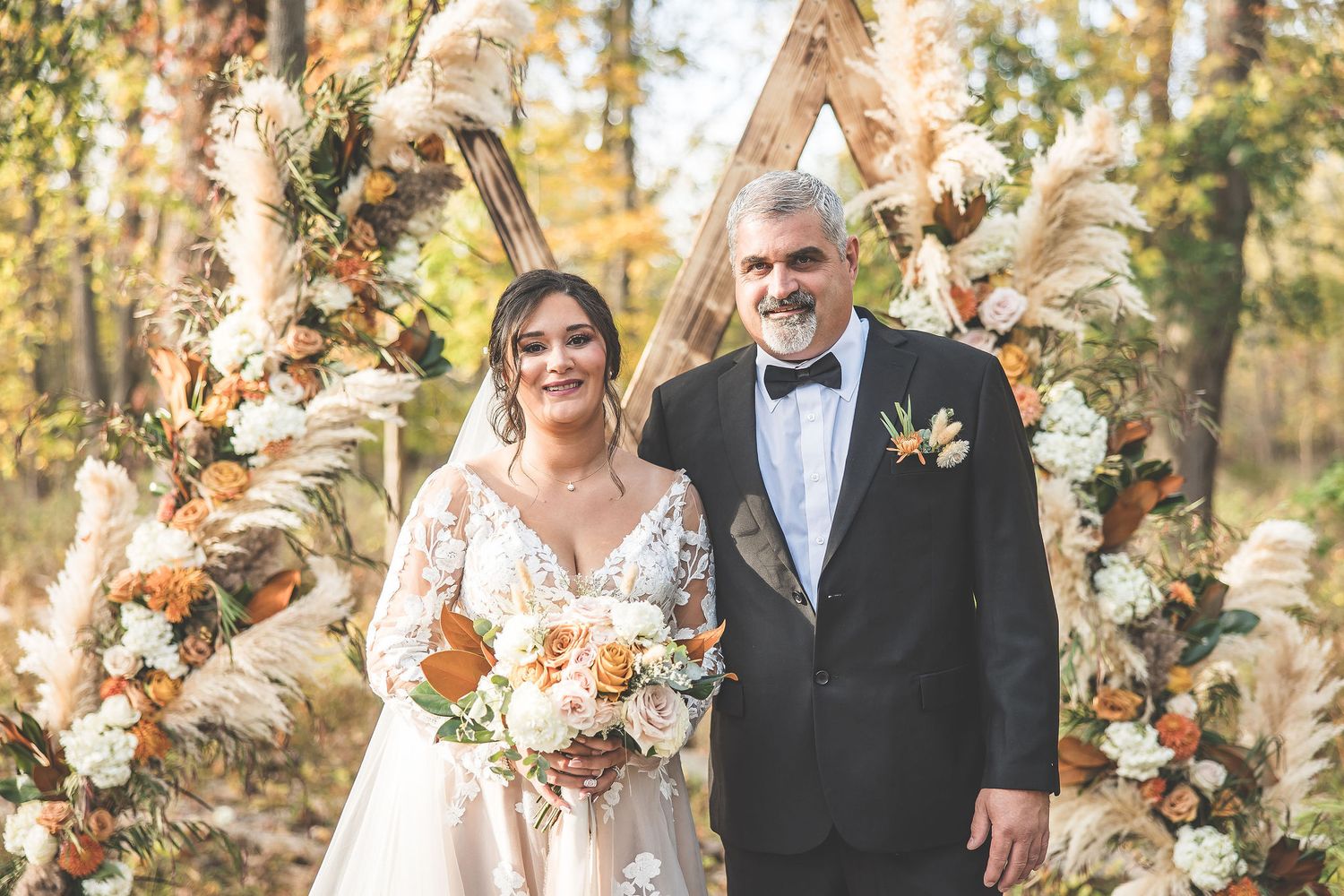 Wedding couple walking through outdoor venue decorated with pampas grass and fall flowers.