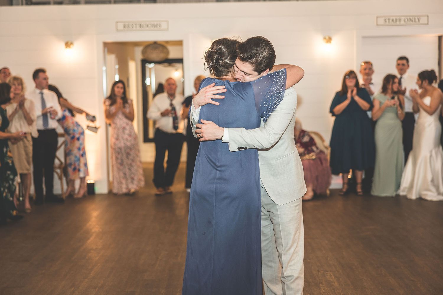 Couples slow dance together at a wedding reception in a warmly lit venue with white walls.