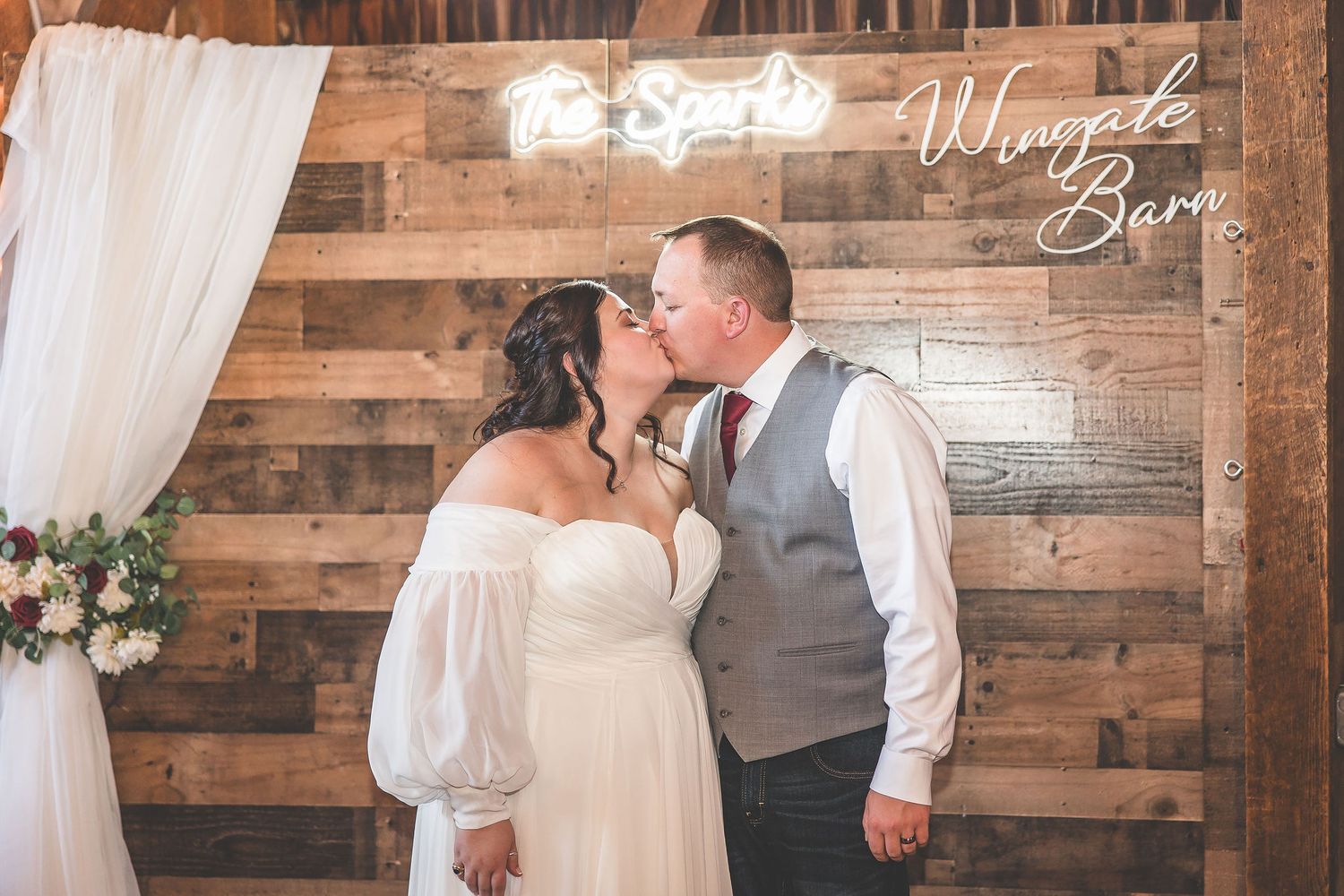 Wedding celebration inside a rustic barn venue with wooden plank walls and white draping.