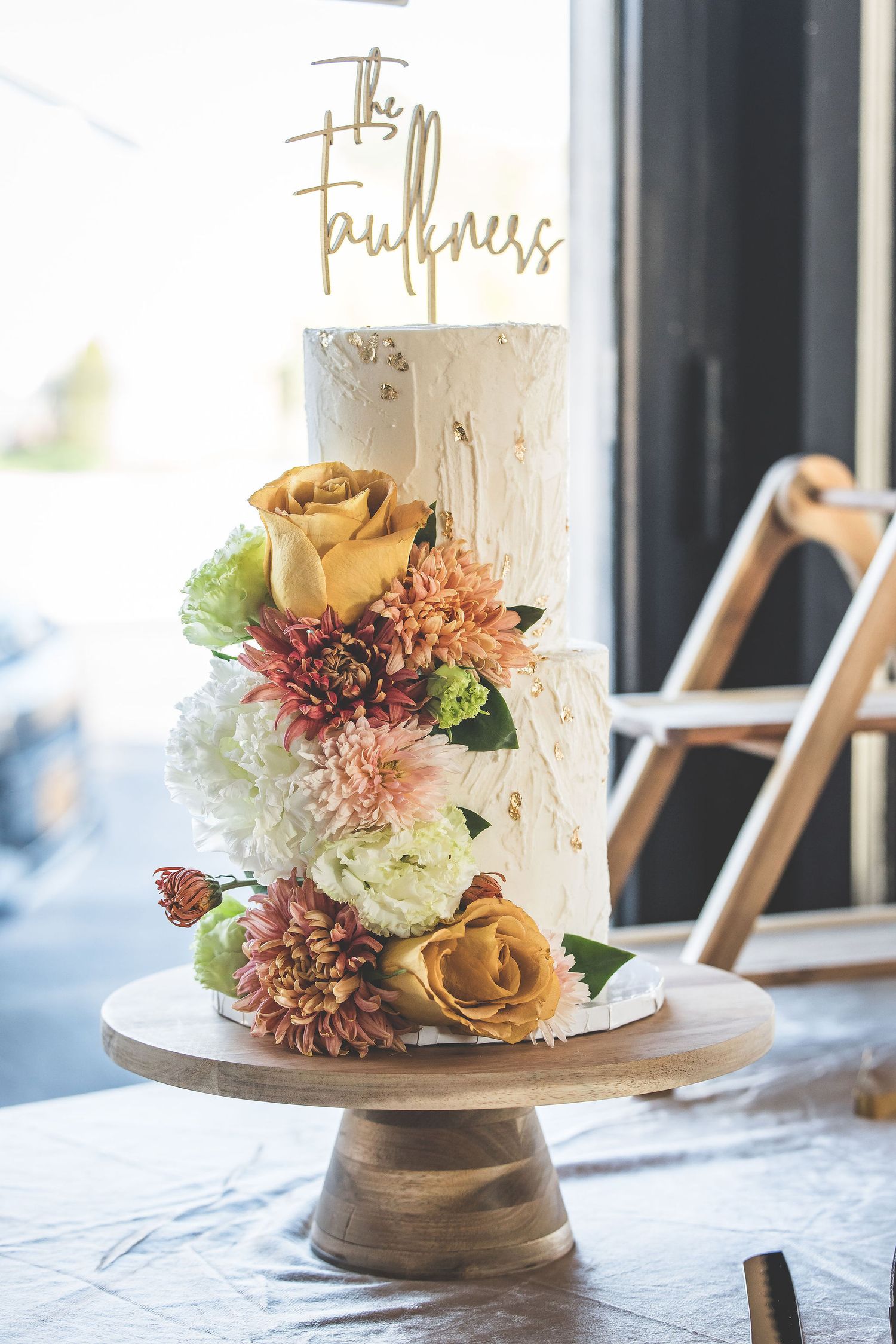 White wedding cake decorated with fresh flowers in pink and peach tones on a wooden cake stand.