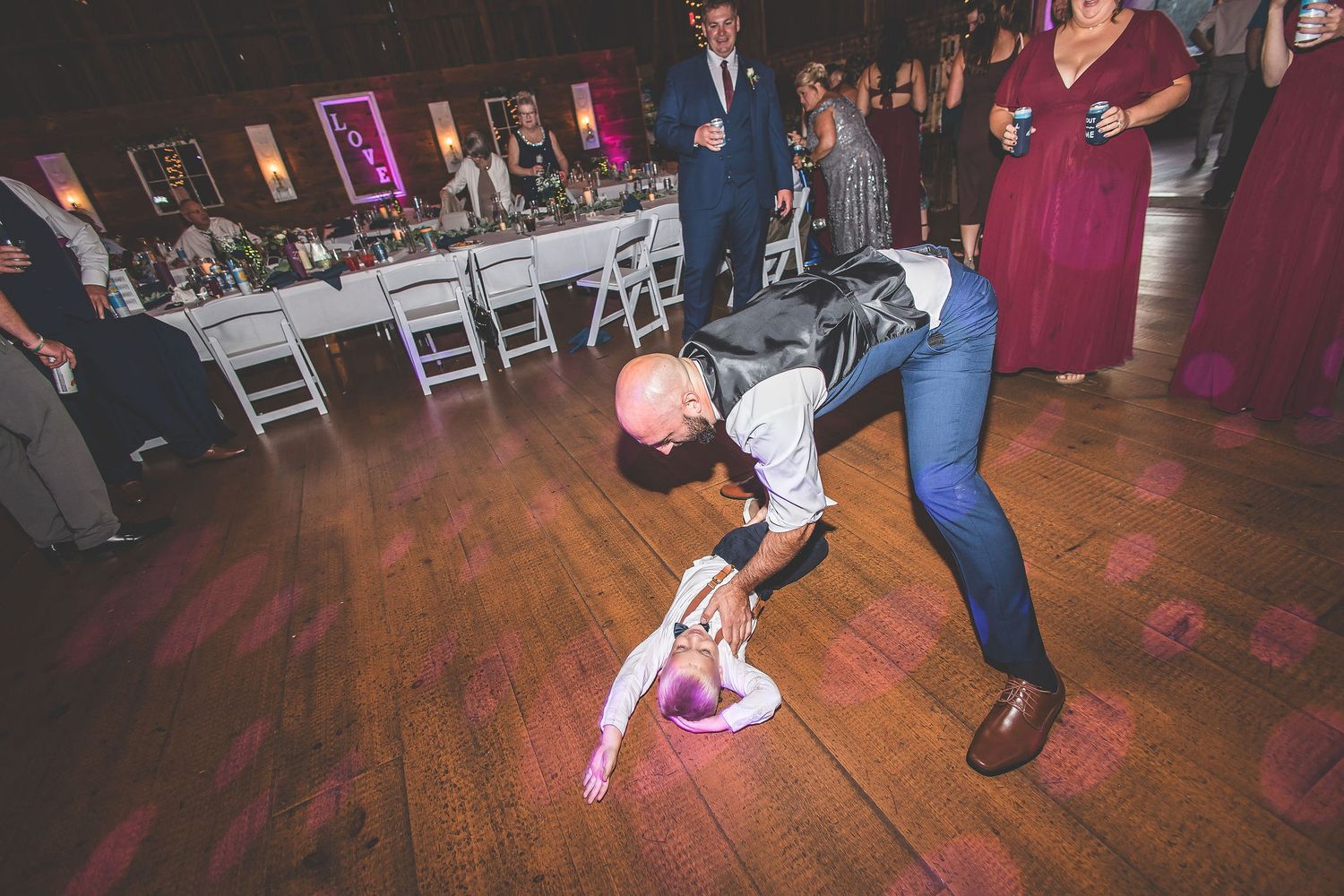 Wedding reception guest performs dramatic dance move on wooden floor.