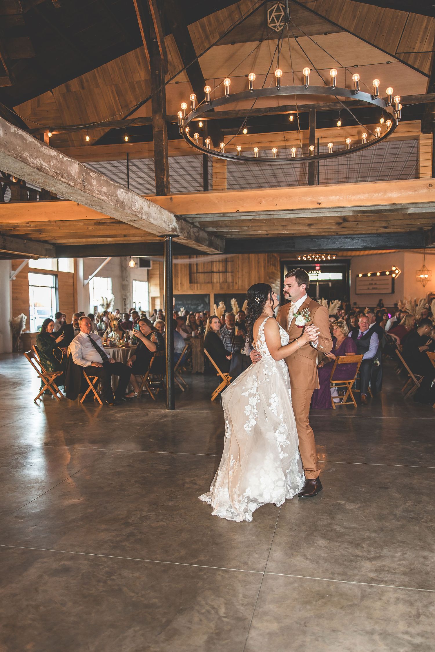 A spacious barn venue with circular chandeliers hosts a wedding reception first dance.