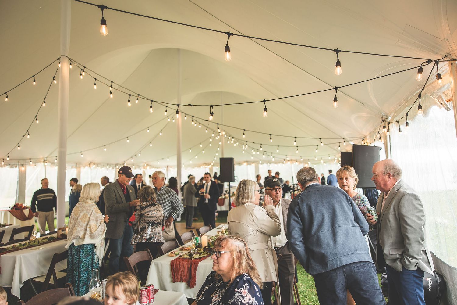 Wedding reception under a white tent with string lights and guests mingling.