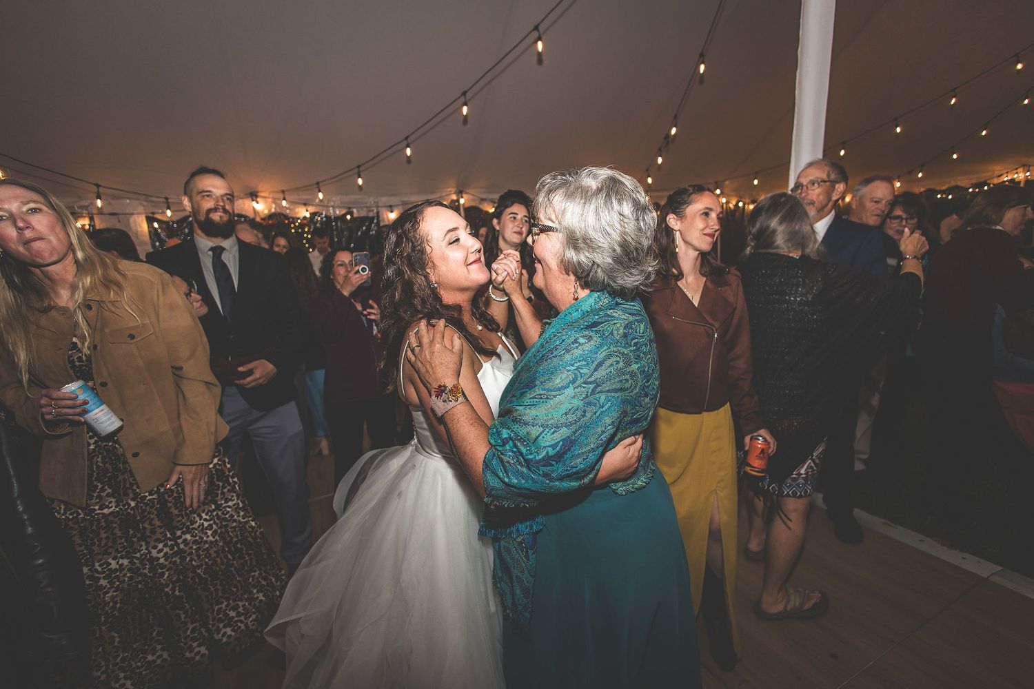Wedding reception dance floor filled with guests celebrating under glowing string lights.