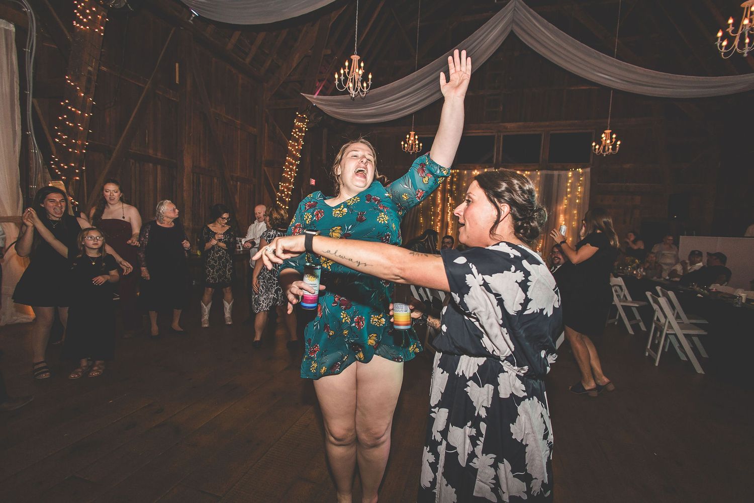 Two party guests dance enthusiastically on a wooden floor under draped fabric and chandeliers.