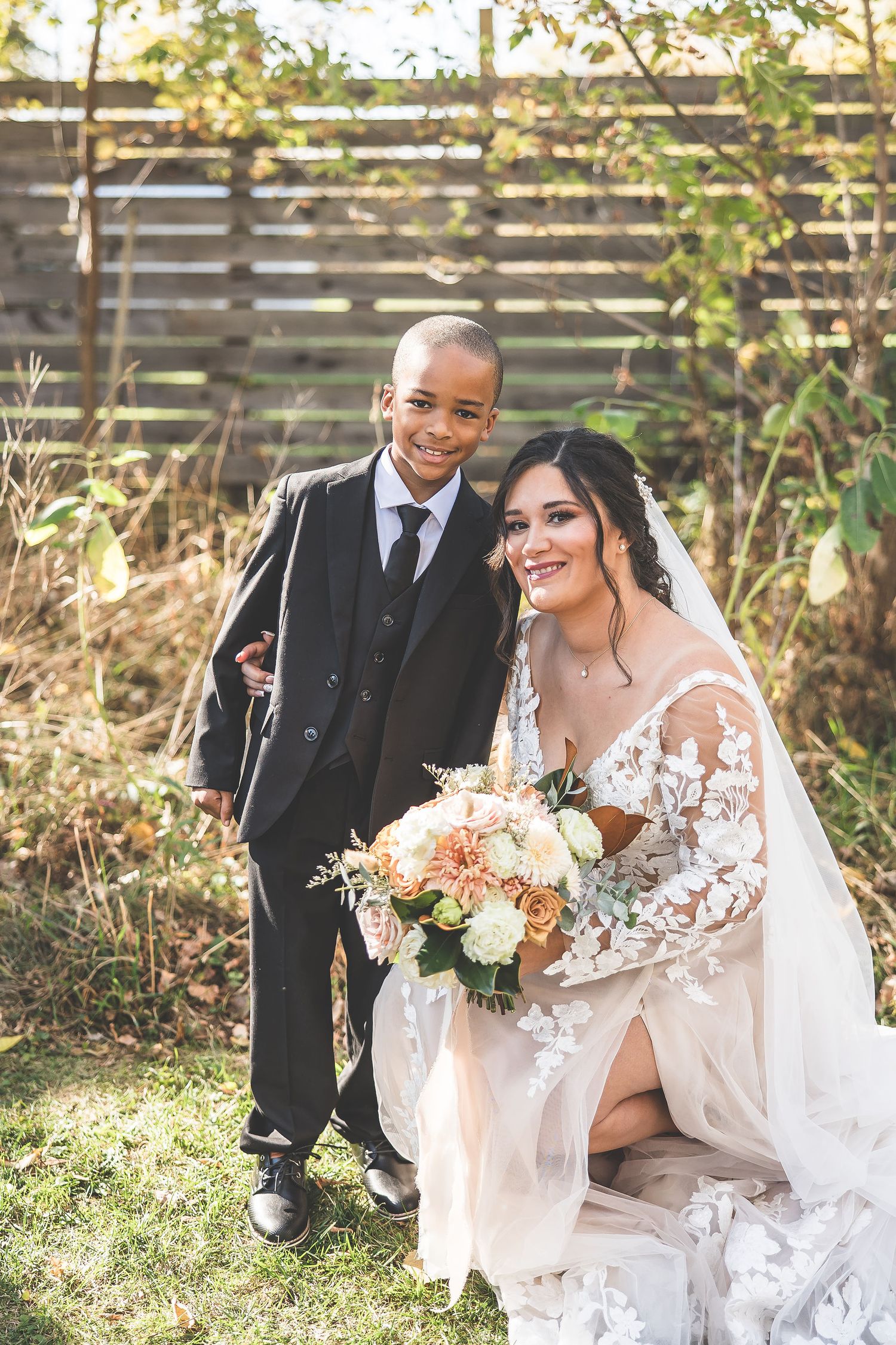 Wedding couple sitting together outdoors holding beautiful peach and white floral bouquets.