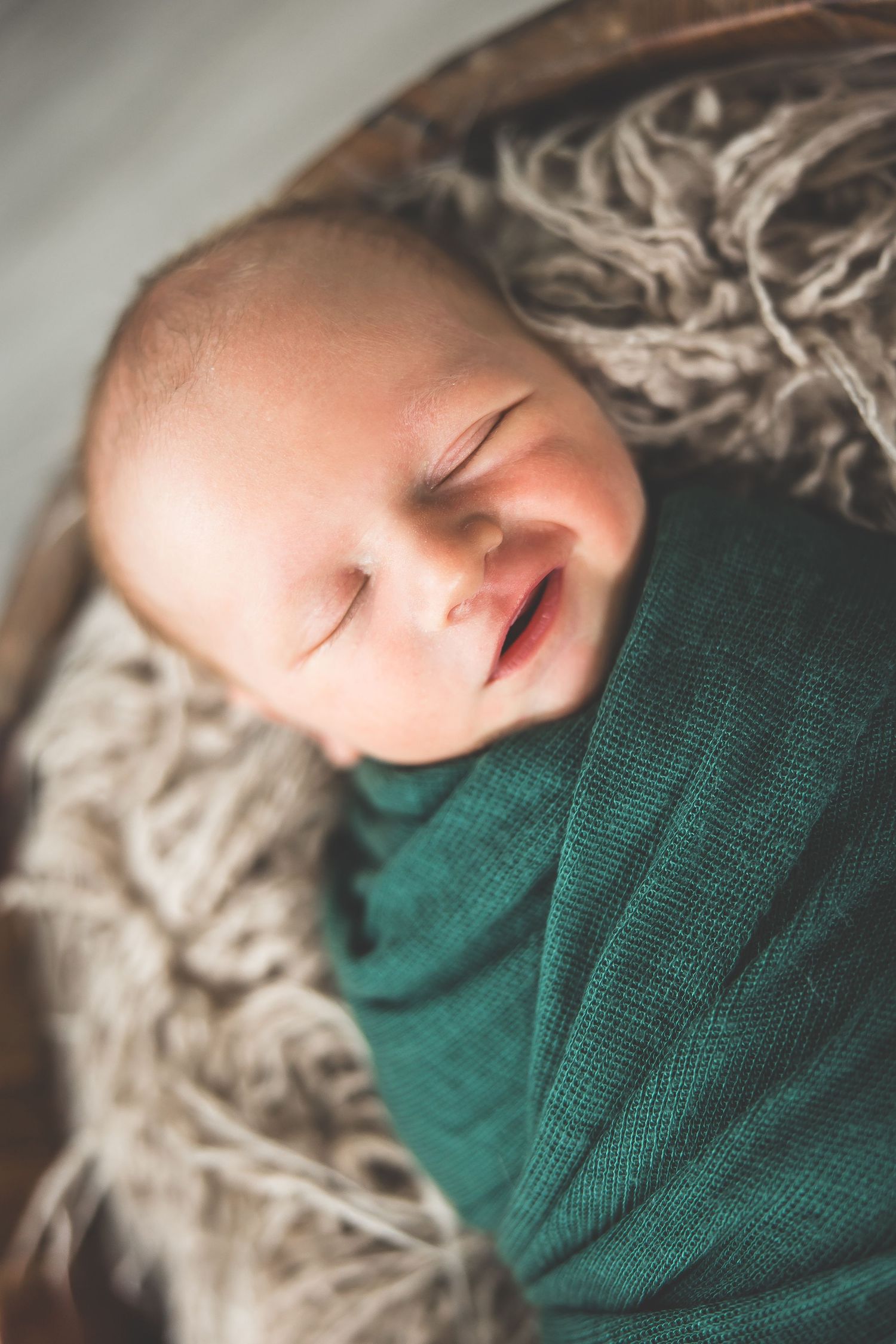 Close-up of a sleeping baby wrapped in a teal swaddle blanket on textured fabric.