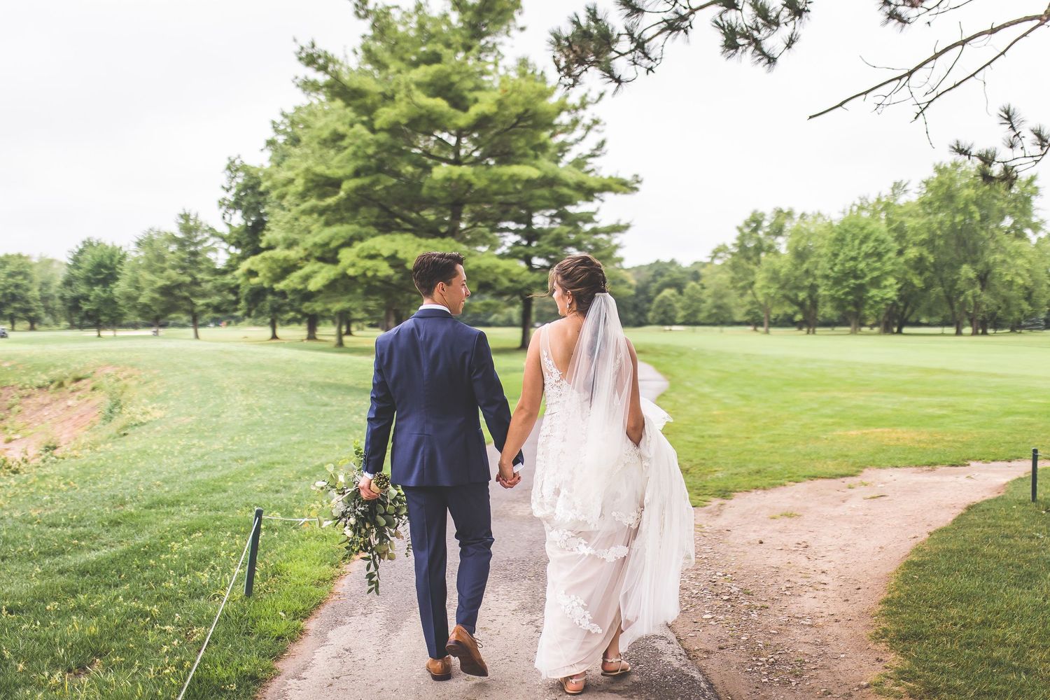 Newlyweds walk hand in hand through a lush green garden path on their wedding day.