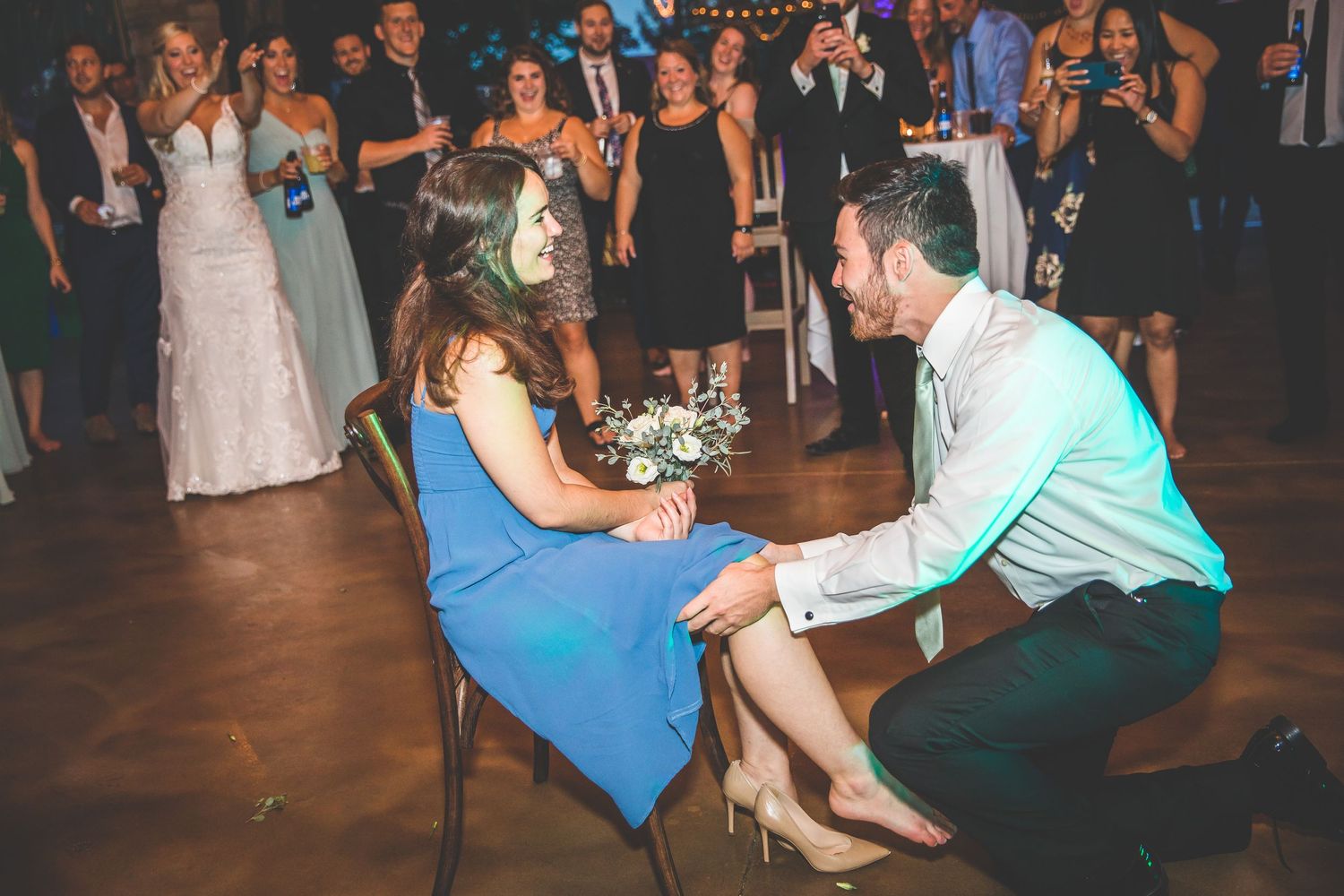 Wedding guest in blue dress participates in traditional garter removal dance.