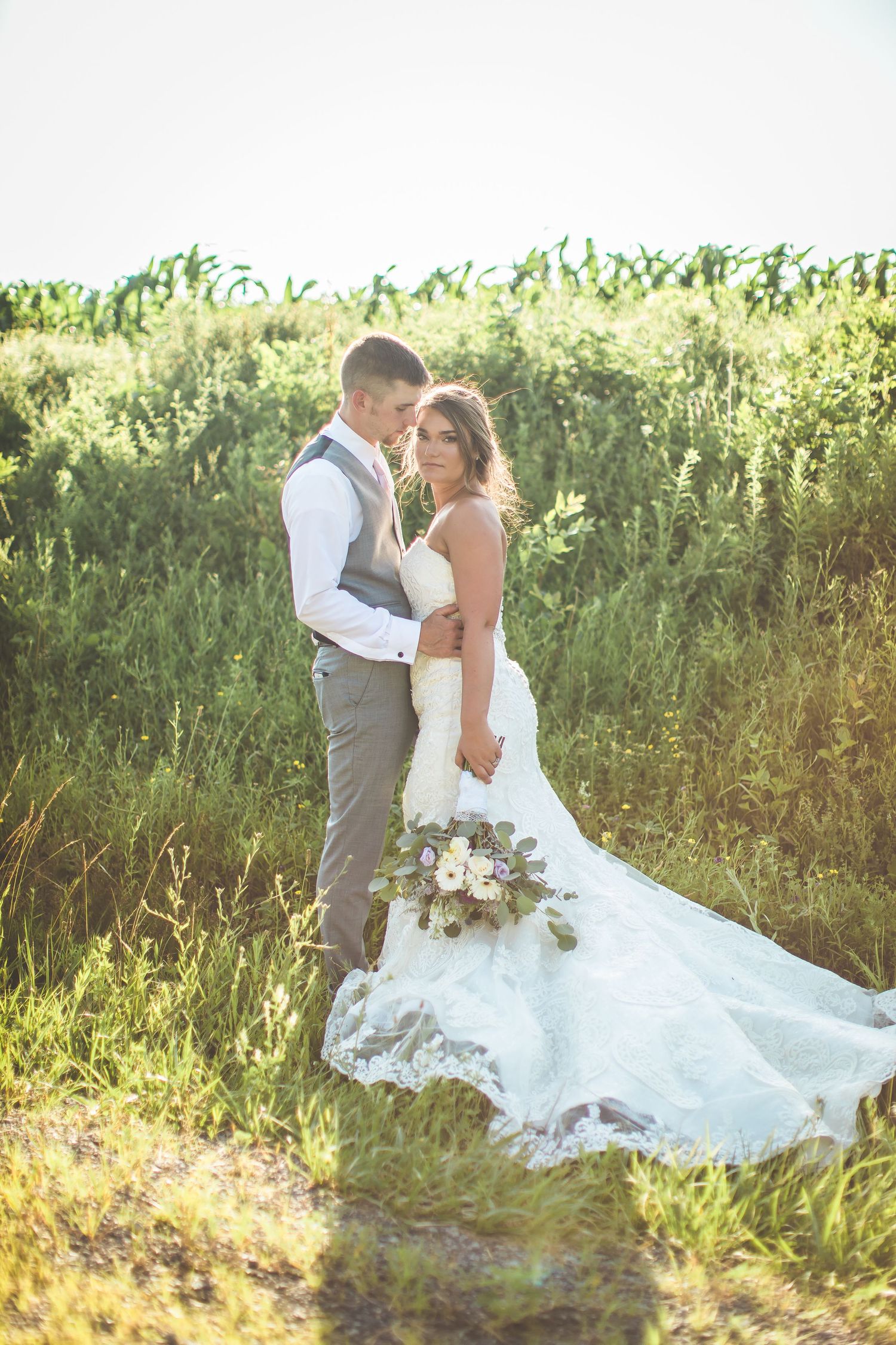 A romantic wedding portrait in a sunlit field with flowing white dress and natural backdrop.
