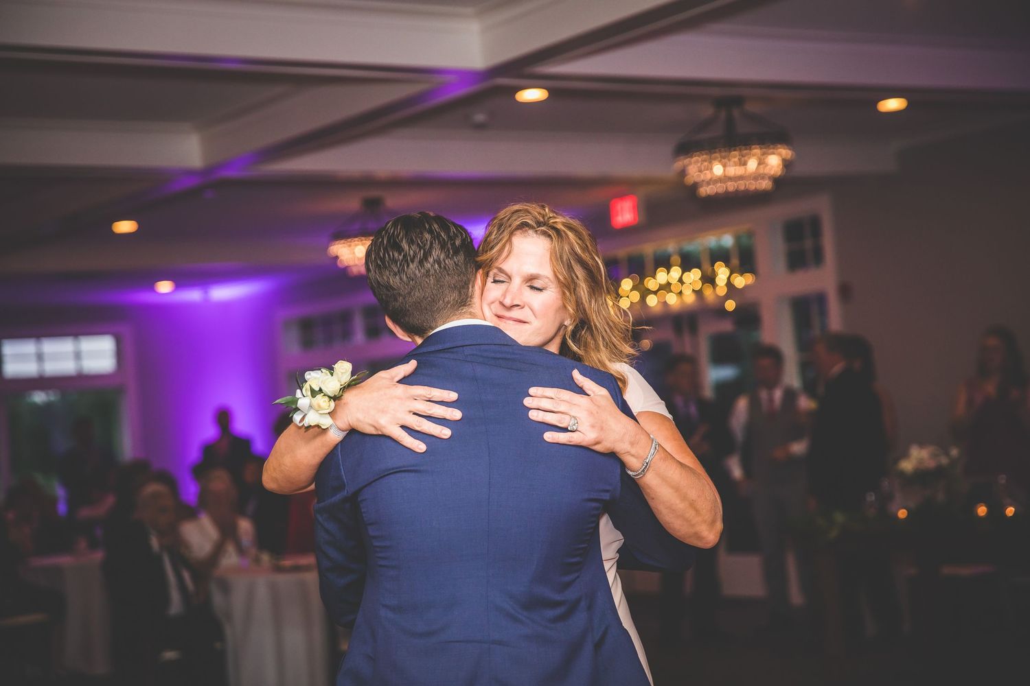 Romantic dance at wedding reception with purple mood lighting and chandelier overhead.