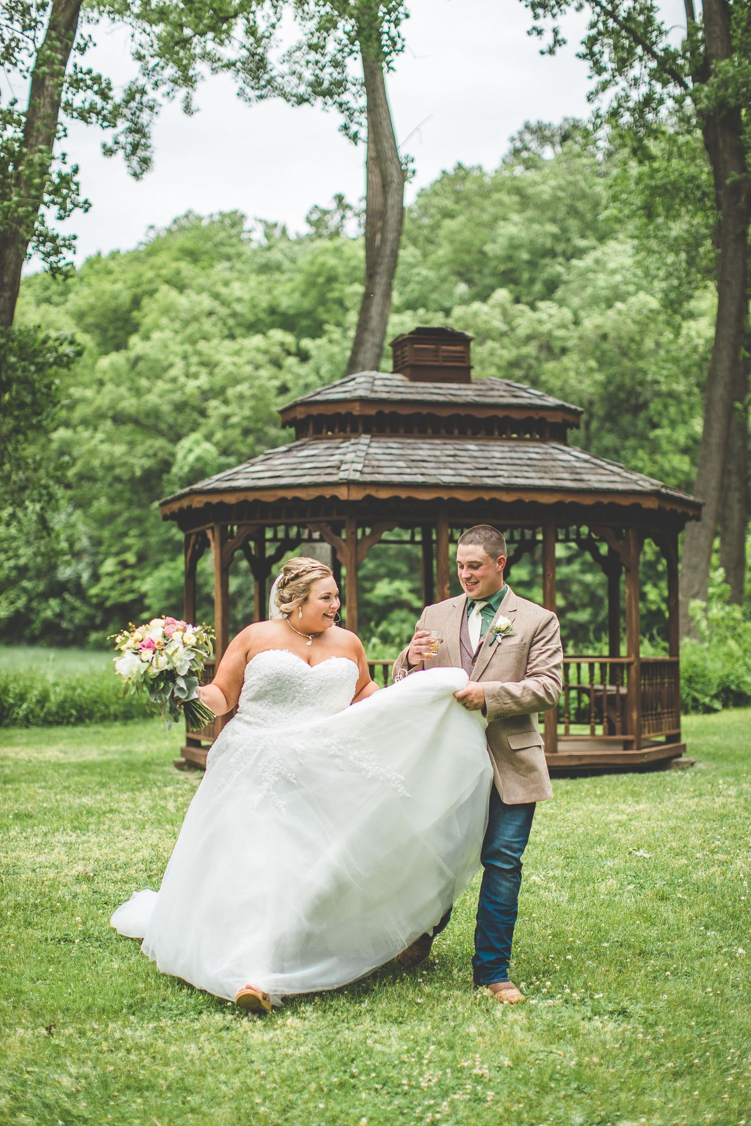 Playful wedding photos taken near a wooden gazebo in a lush green garden setting.