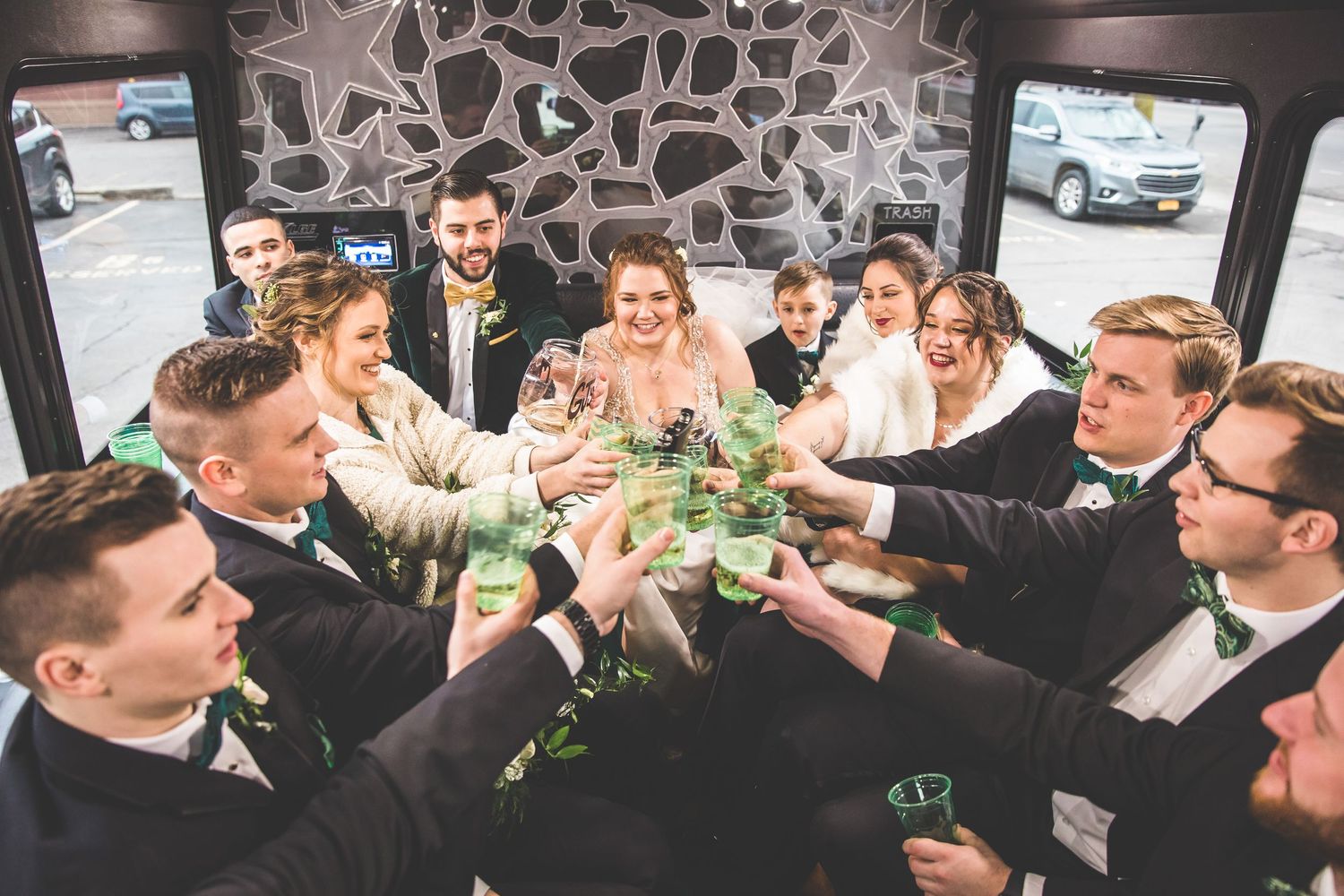 Wedding party toasting with drinks inside a vehicle during celebration.