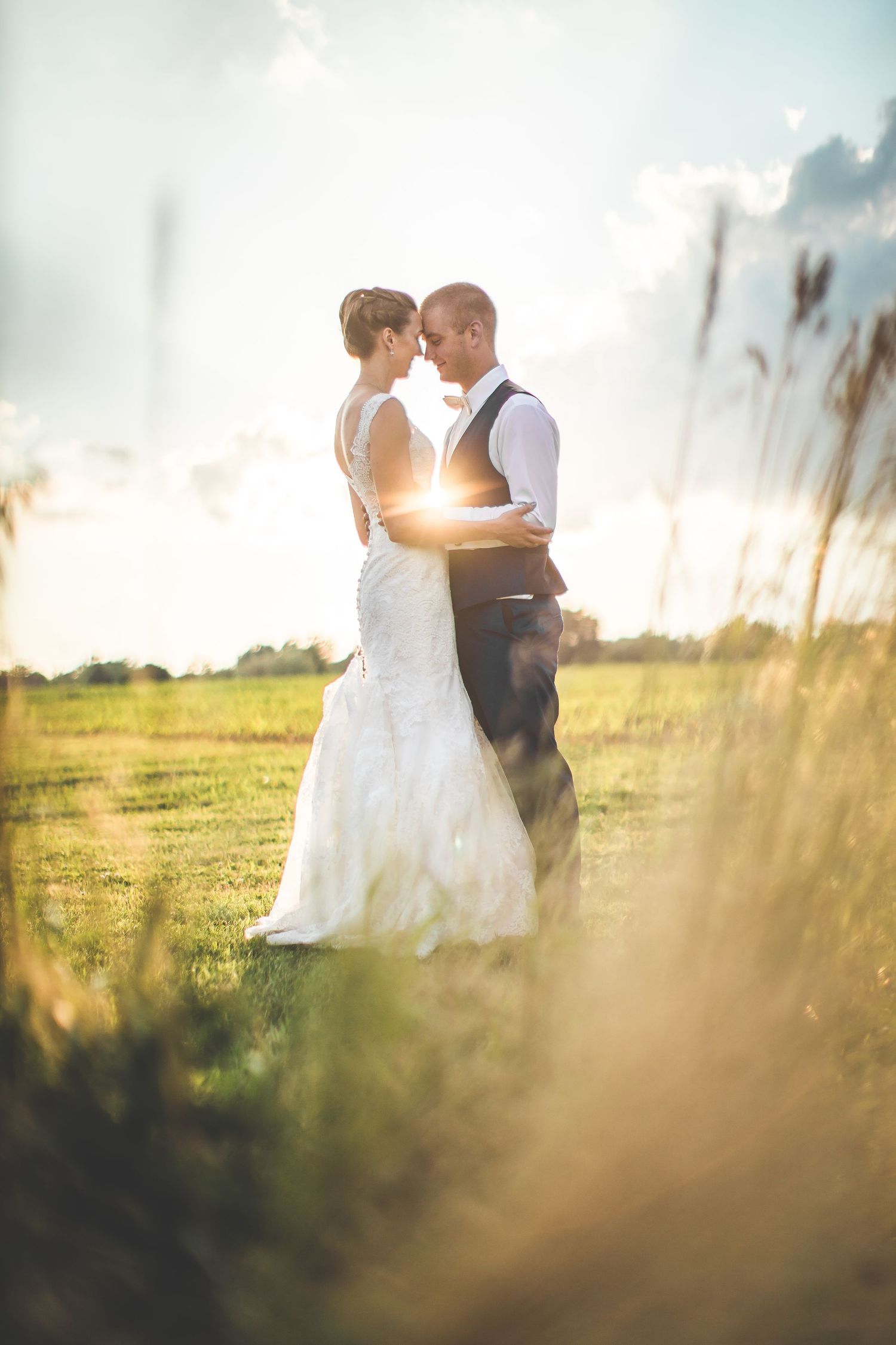 Romantic sunset wedding portraits in a field with tall grass and dreamy lighting.