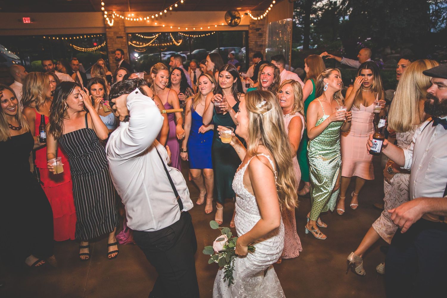 Crowded dance floor at wedding reception with guests celebrating under festive lighting.