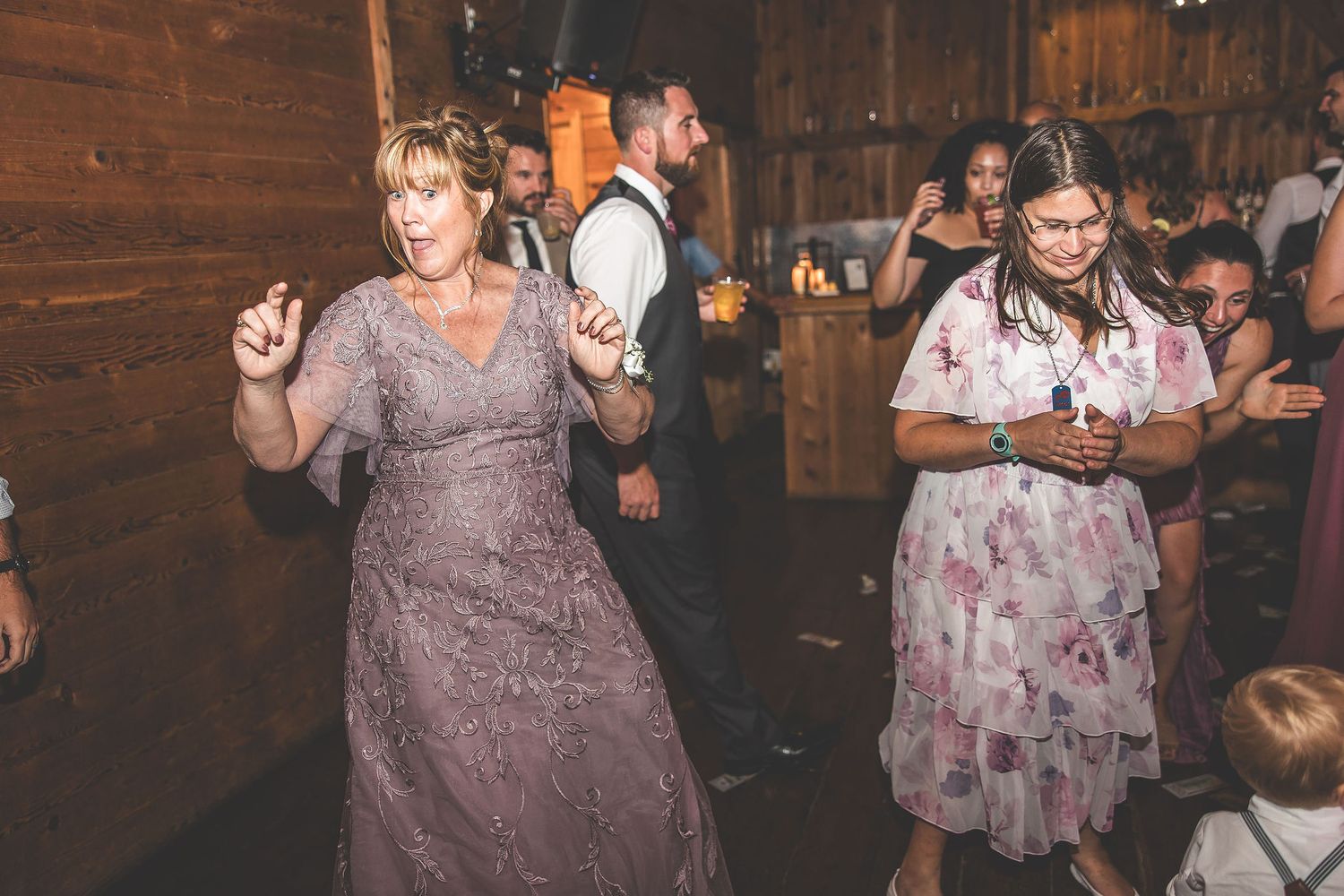 Wedding guests dancing in rustic wood-paneled reception venue.