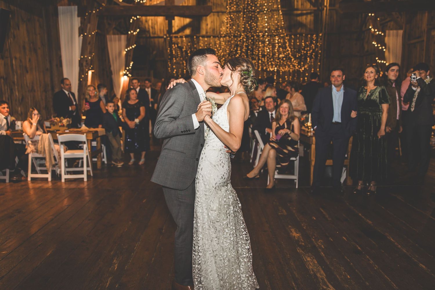 Newlyweds dance together during reception in rustic wooden barn with warm lighting.
