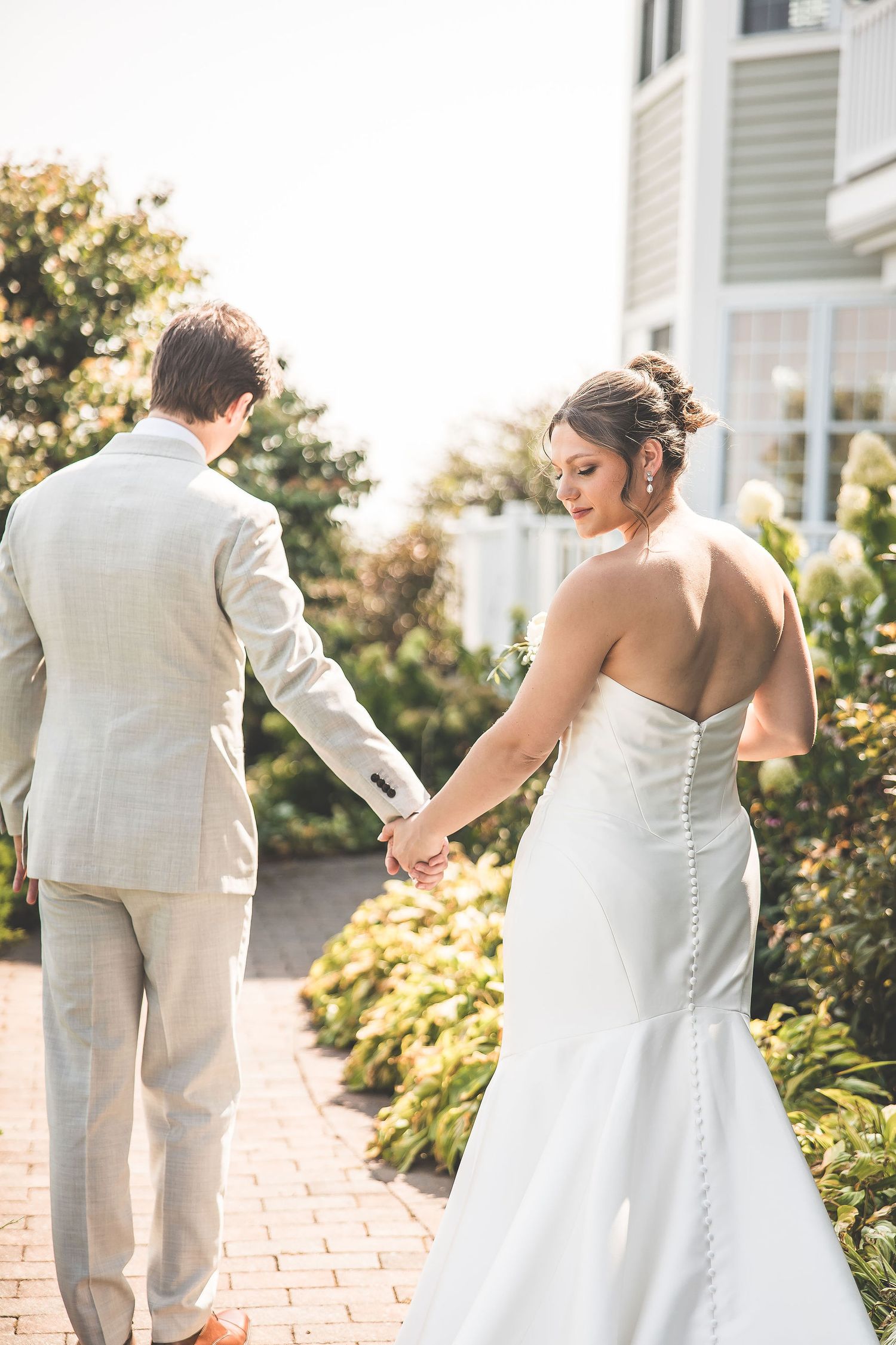 Candid wedding moments captured on brick pathway beside elegant home.