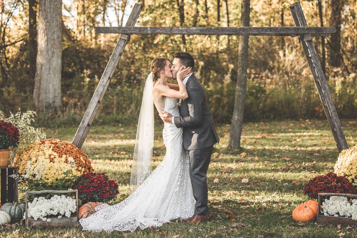 A fall wedding ceremony in a wooded setting decorated with orange pumpkins and burgundy floral arrangements.
