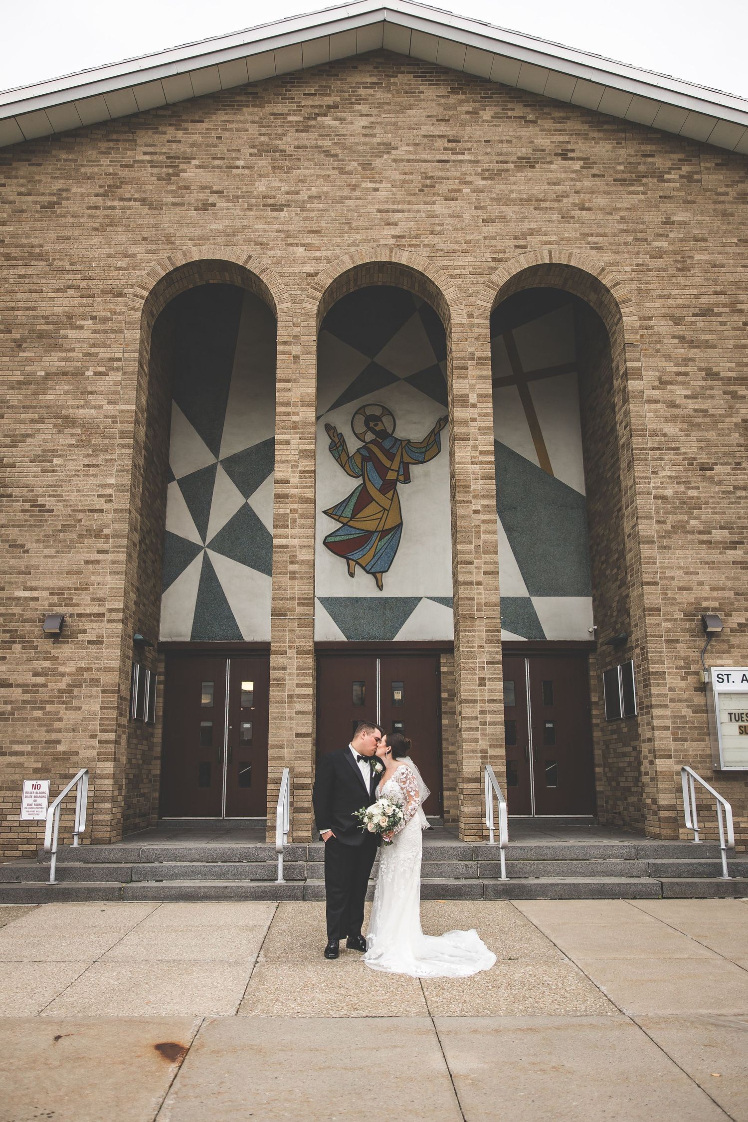 Newlyweds stand before brick church facade featuring artistic stained glass window designs.
