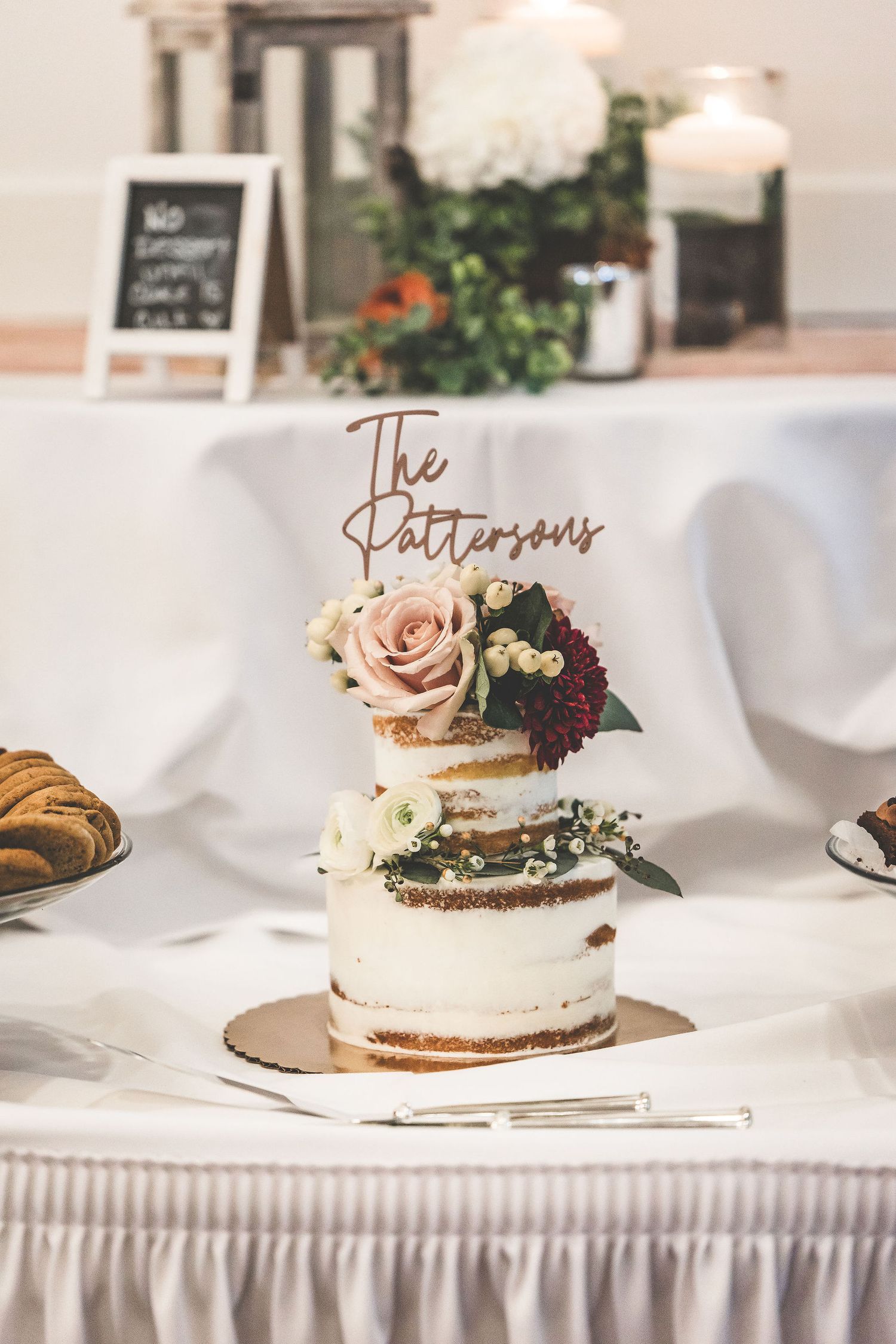 Elegant wedding reception table with decorated naked cake and rose gold details on white tablecloth.