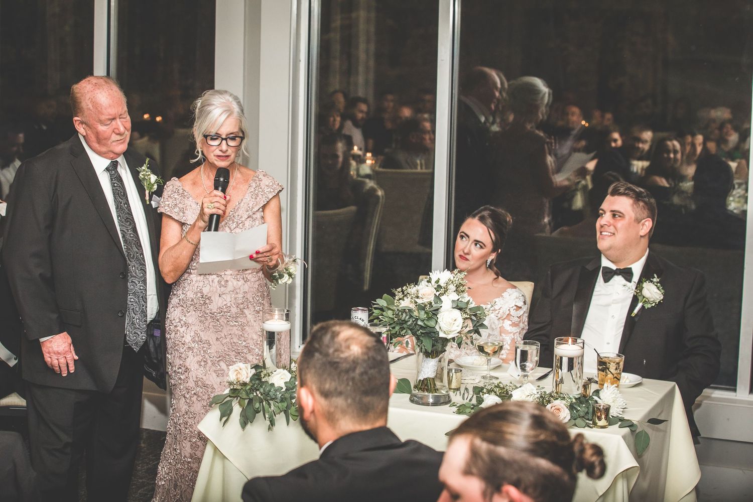 Wedding reception guests enjoy dinner and conversation at elegantly decorated tables.