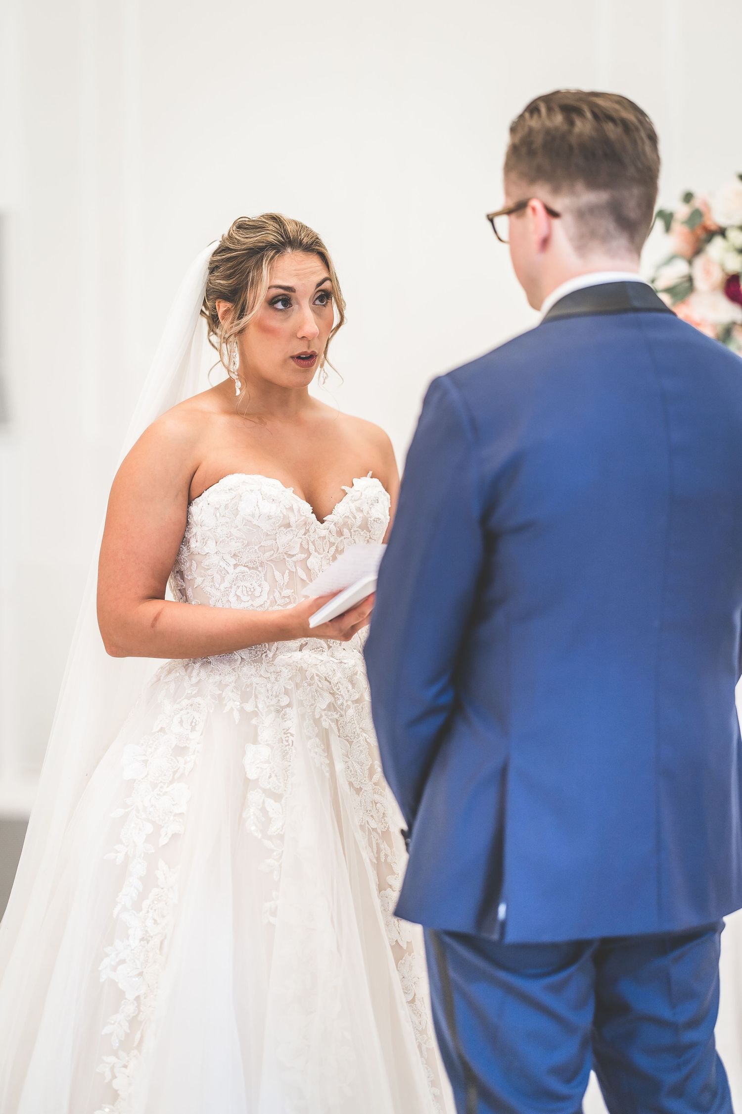 An intimate moment during wedding vows with bride in lace gown and groom in navy suit.