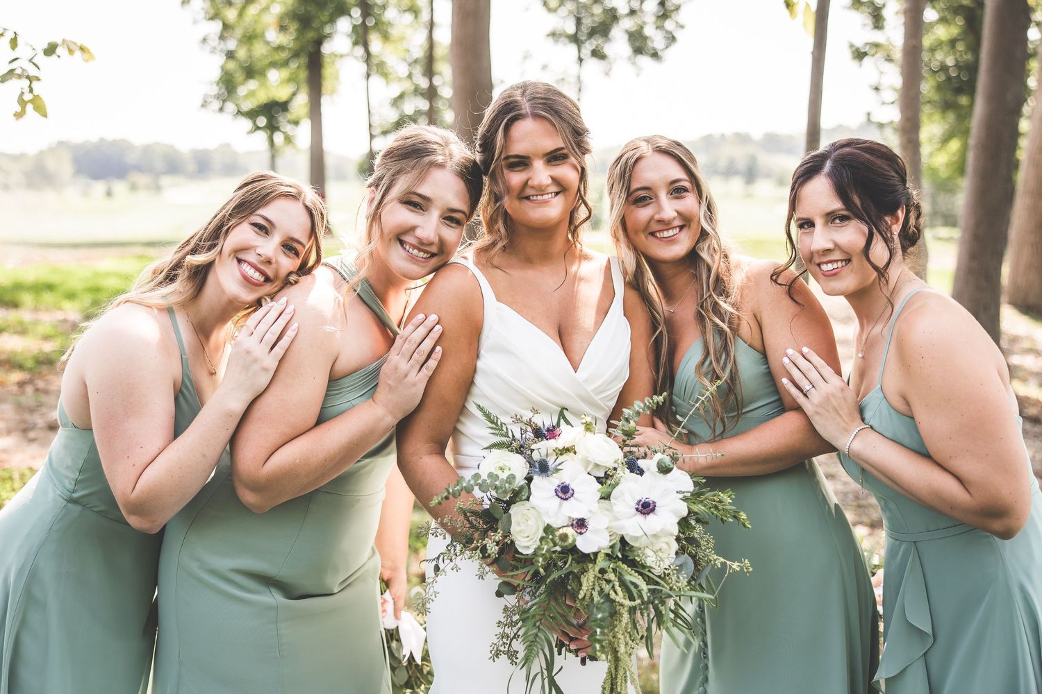 Bridesmaids in sage green dresses share joyful moments together during outdoor wedding photos.