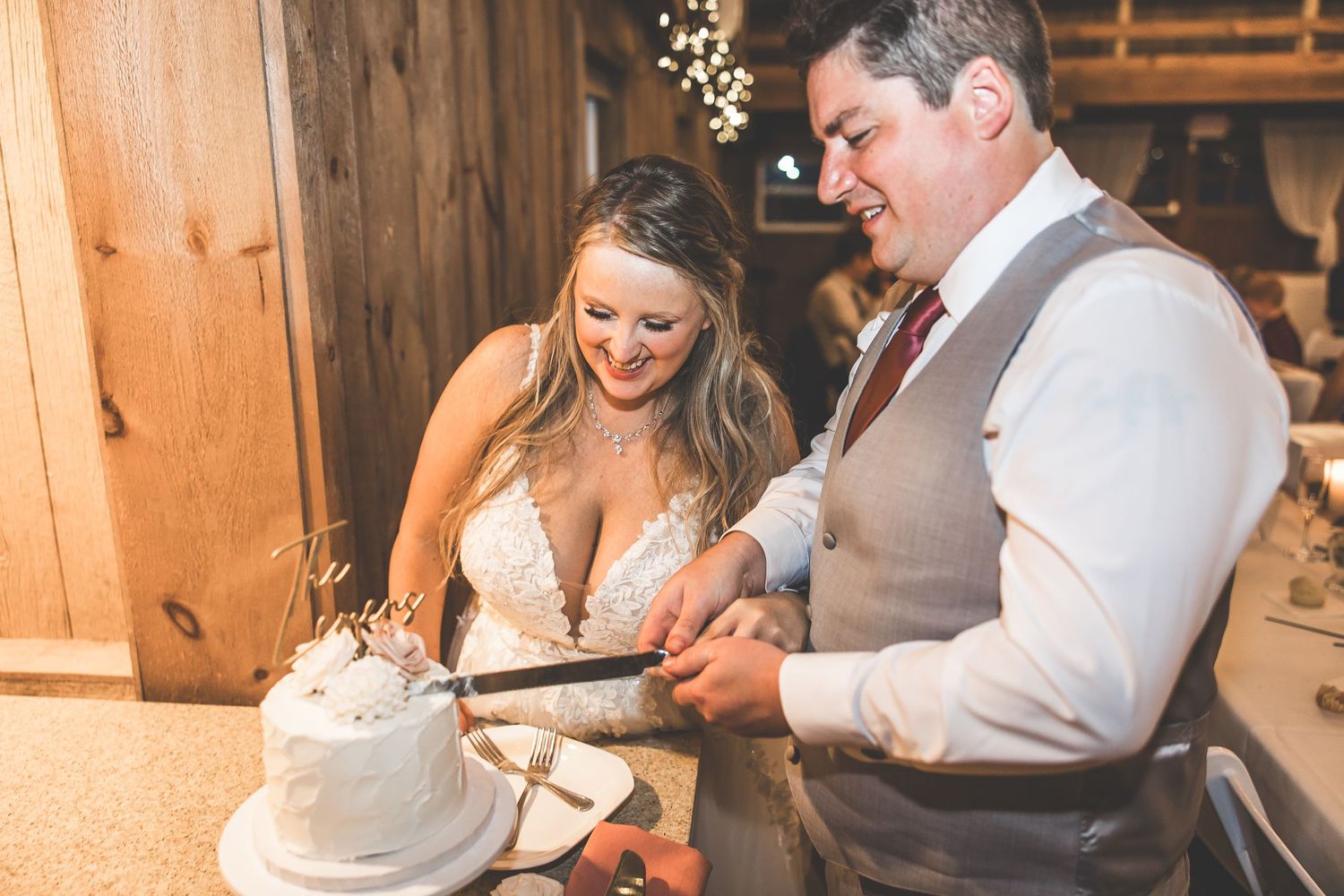Couple cutting their white wedding cake together at rustic barn reception.