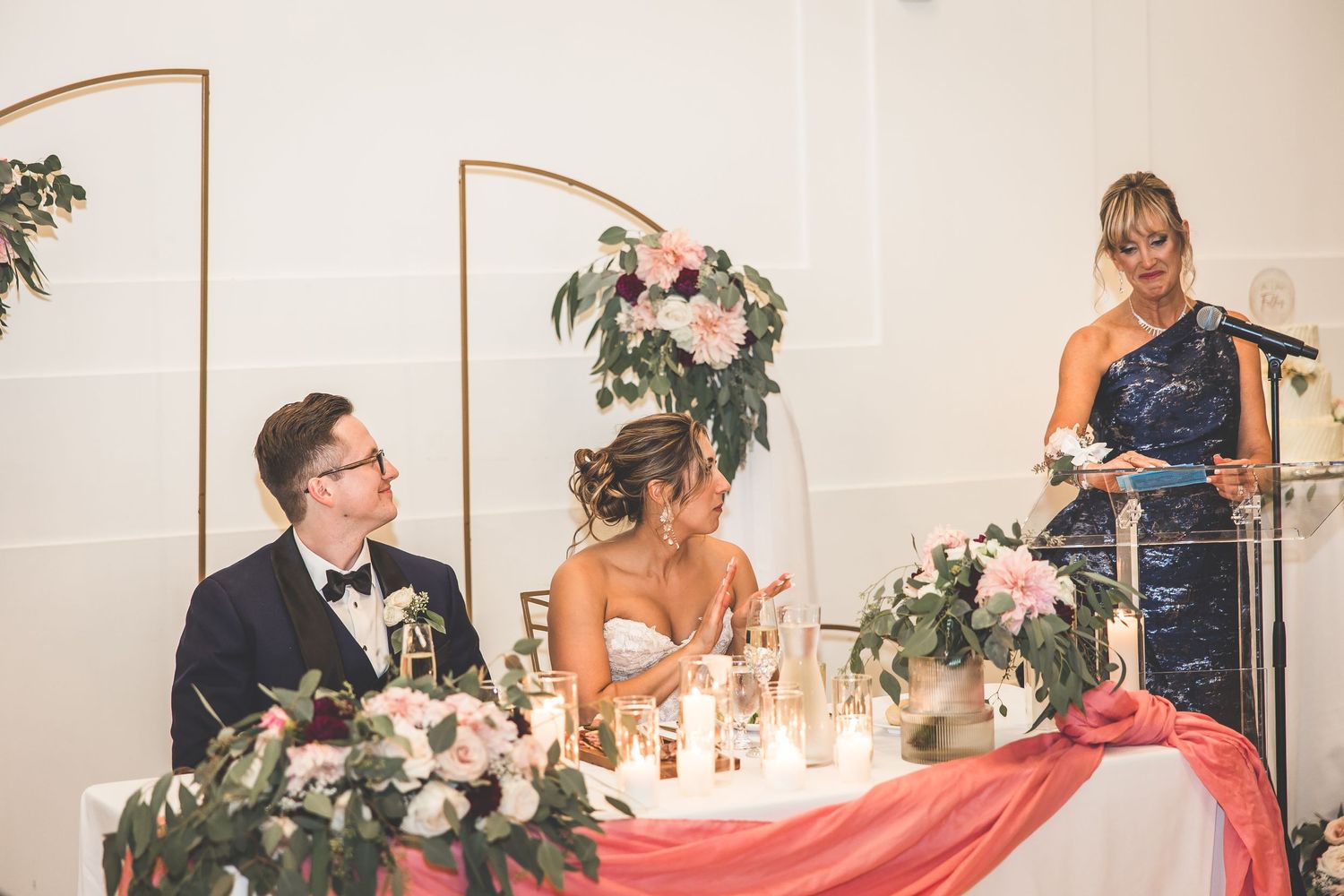 Wedding reception table setup with pink and white floral centerpieces and romantic lighting.