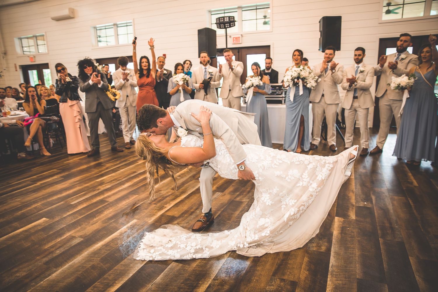 Wedding couple performs a dramatic dance move on wooden floors as guests cheer.