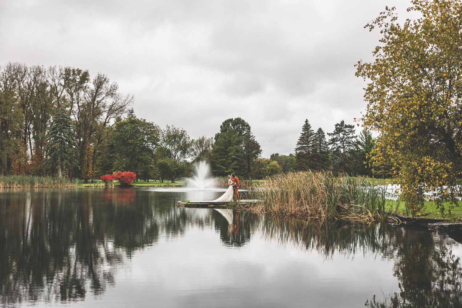 Scenic lake view with fountain spray and autumn foliage reflecting in calm waters.