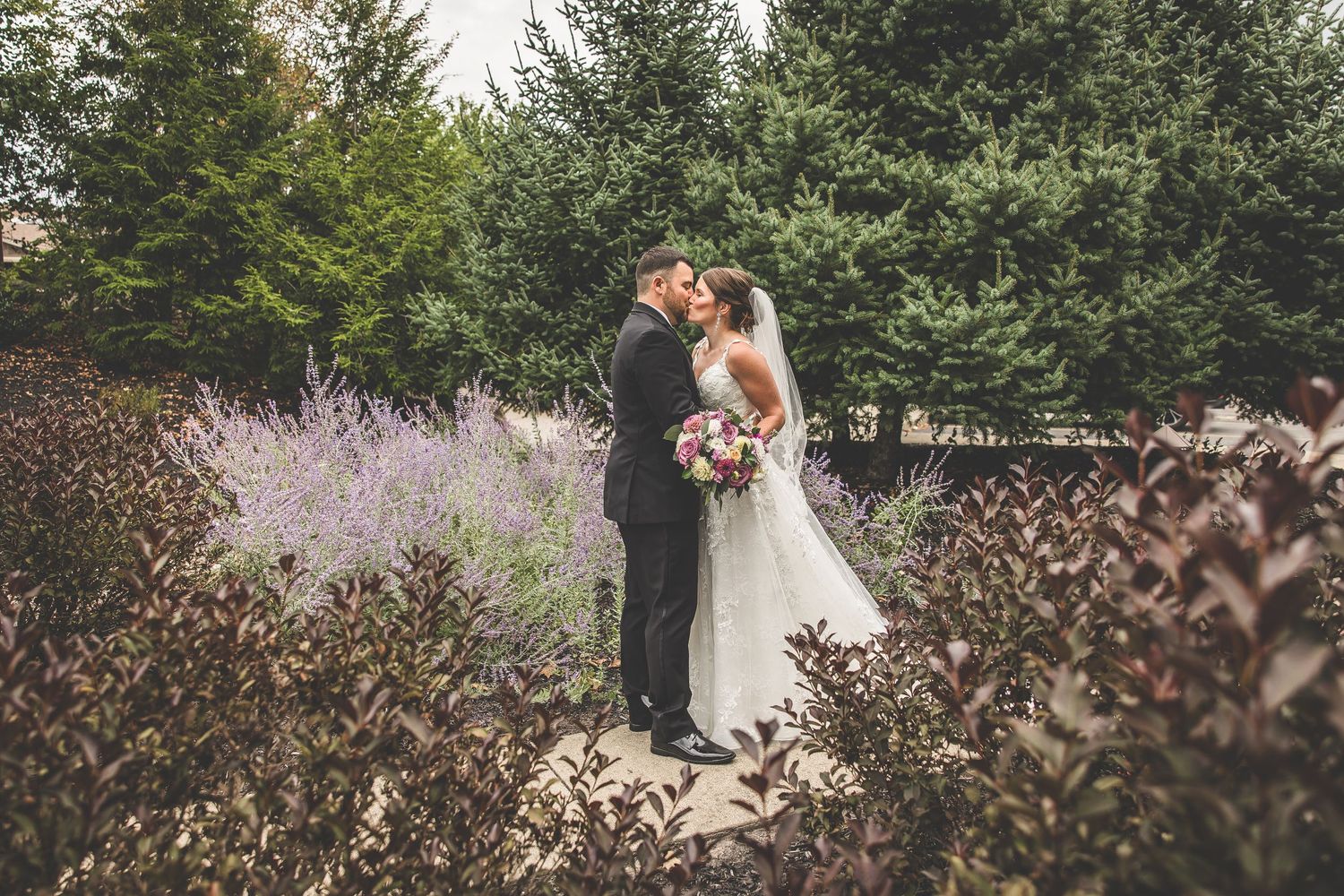 Wedding couple walks together through a scenic garden path with blooming flowers.