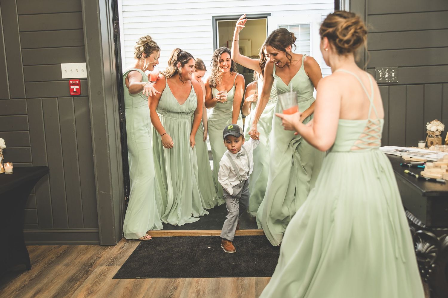 Wedding party in sage green dresses dancing and celebrating at an indoor reception venue.