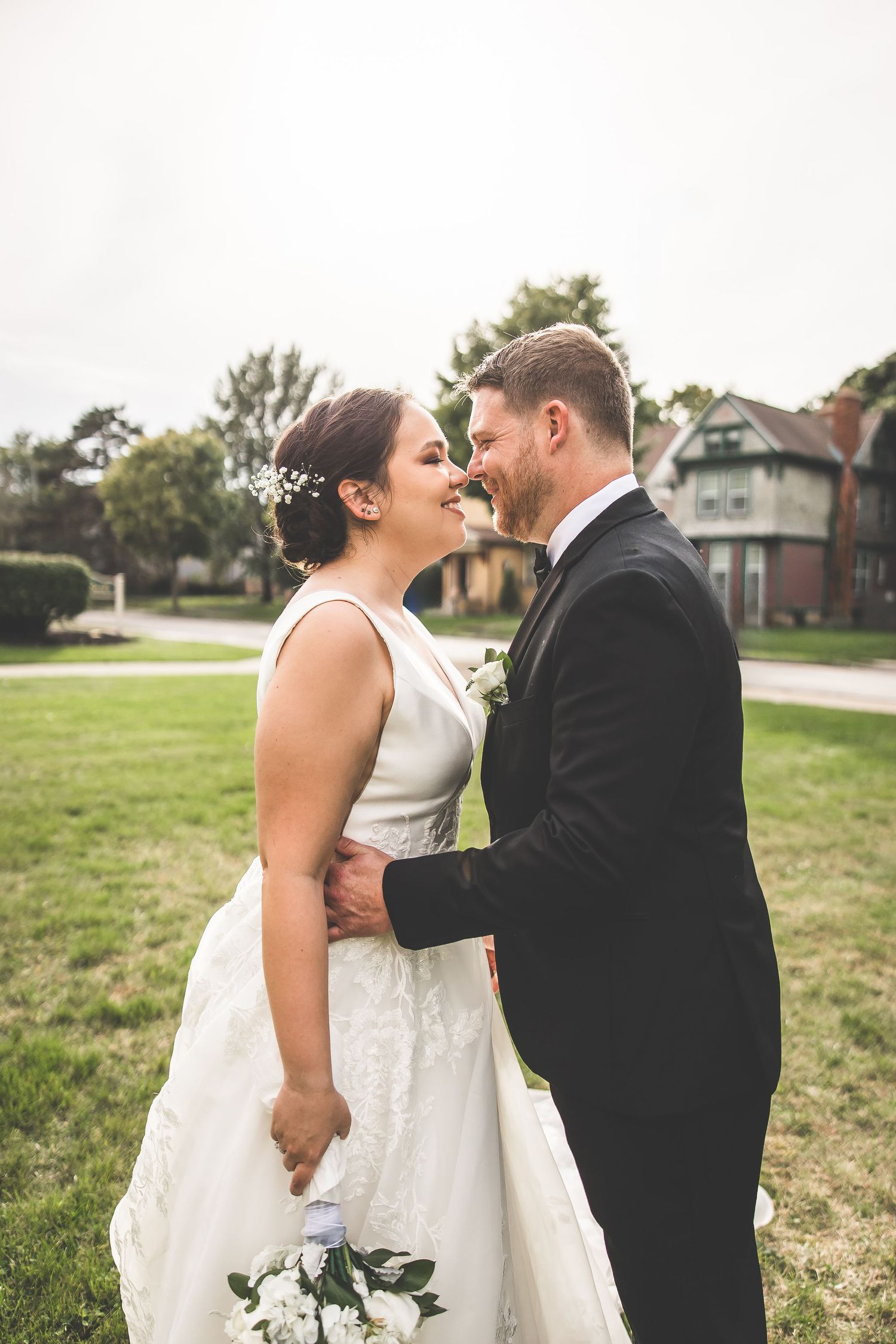 Joyful wedding couple shares intimate moment on grassy lawn during outdoor celebration.