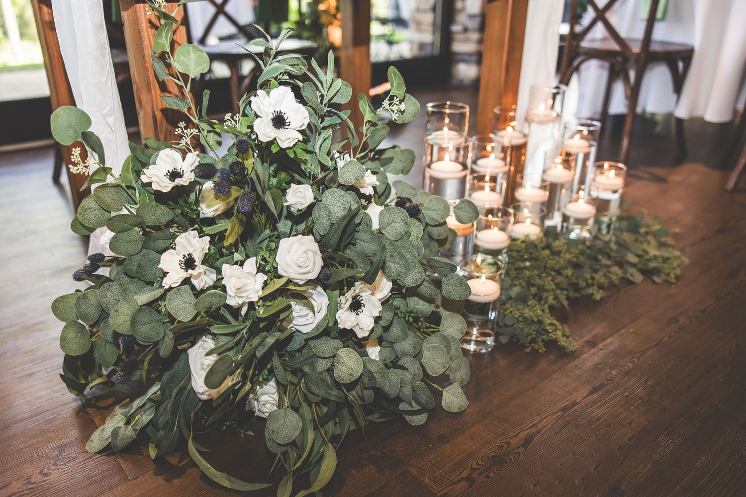 Lush greenery and white floral centerpieces arranged on wedding reception tables.