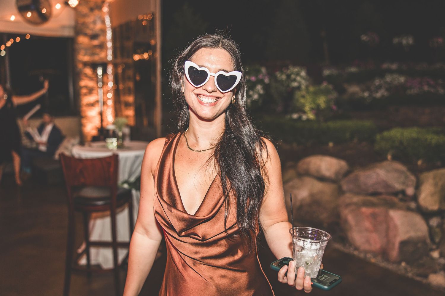 Wedding guests dance and celebrate at a lively reception with string lights and brick walls in the background.