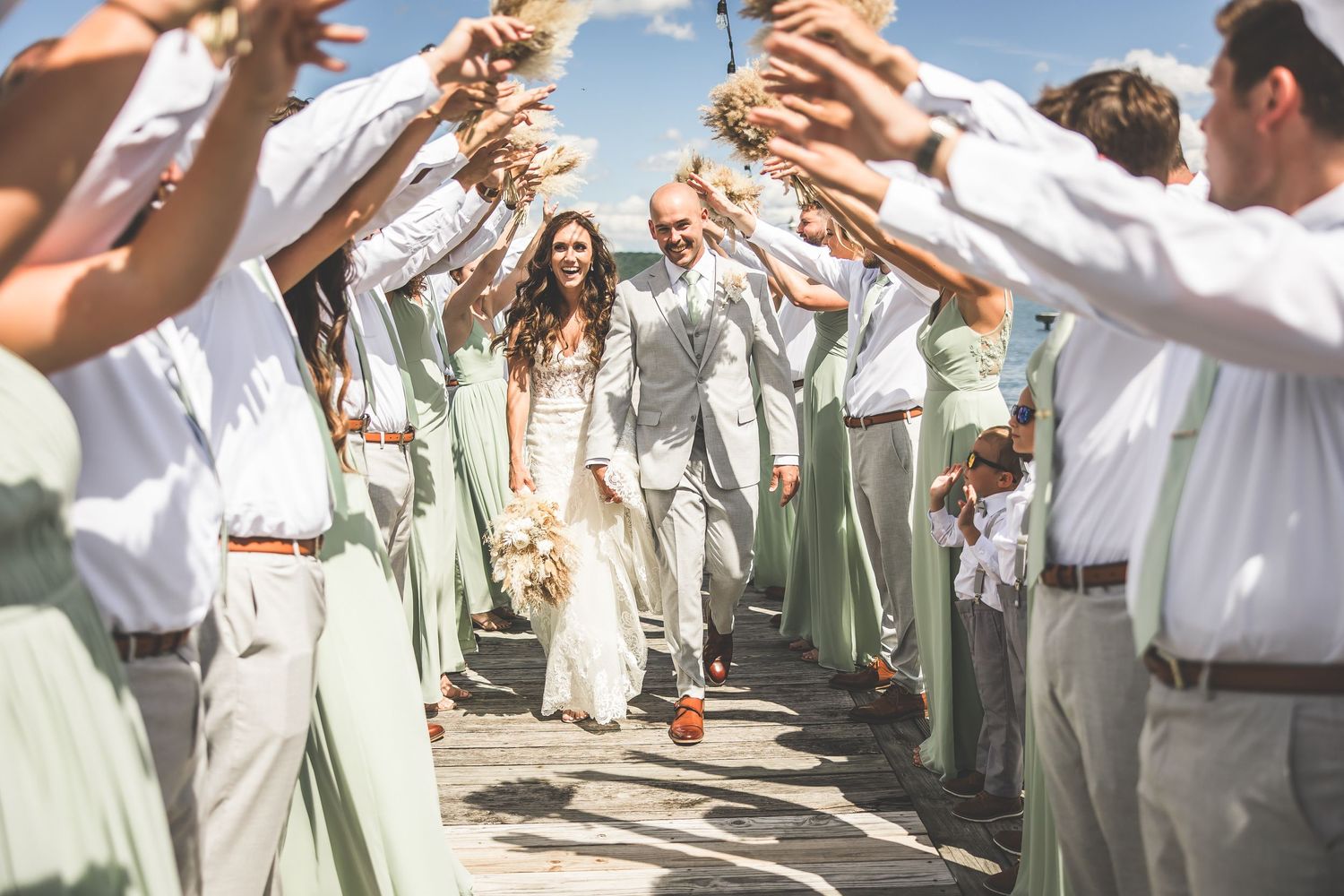 Wedding party forms celebratory tunnel with raised arms as couple walks through.