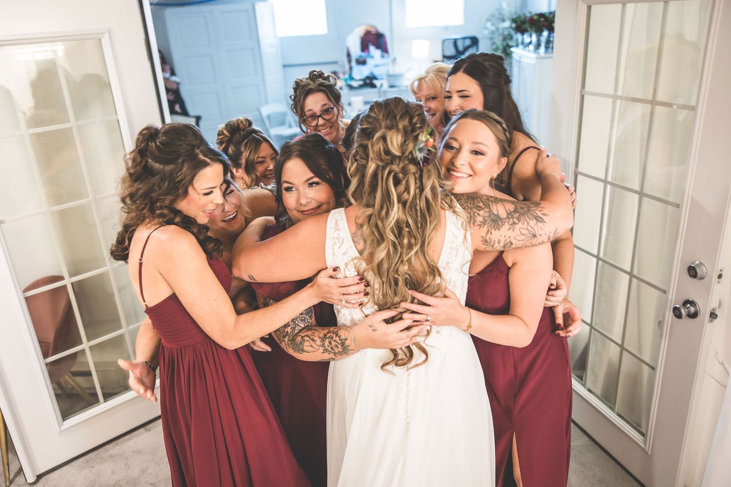 Emotional bridesmaids in burgundy dresses embrace during a special wedding moment.