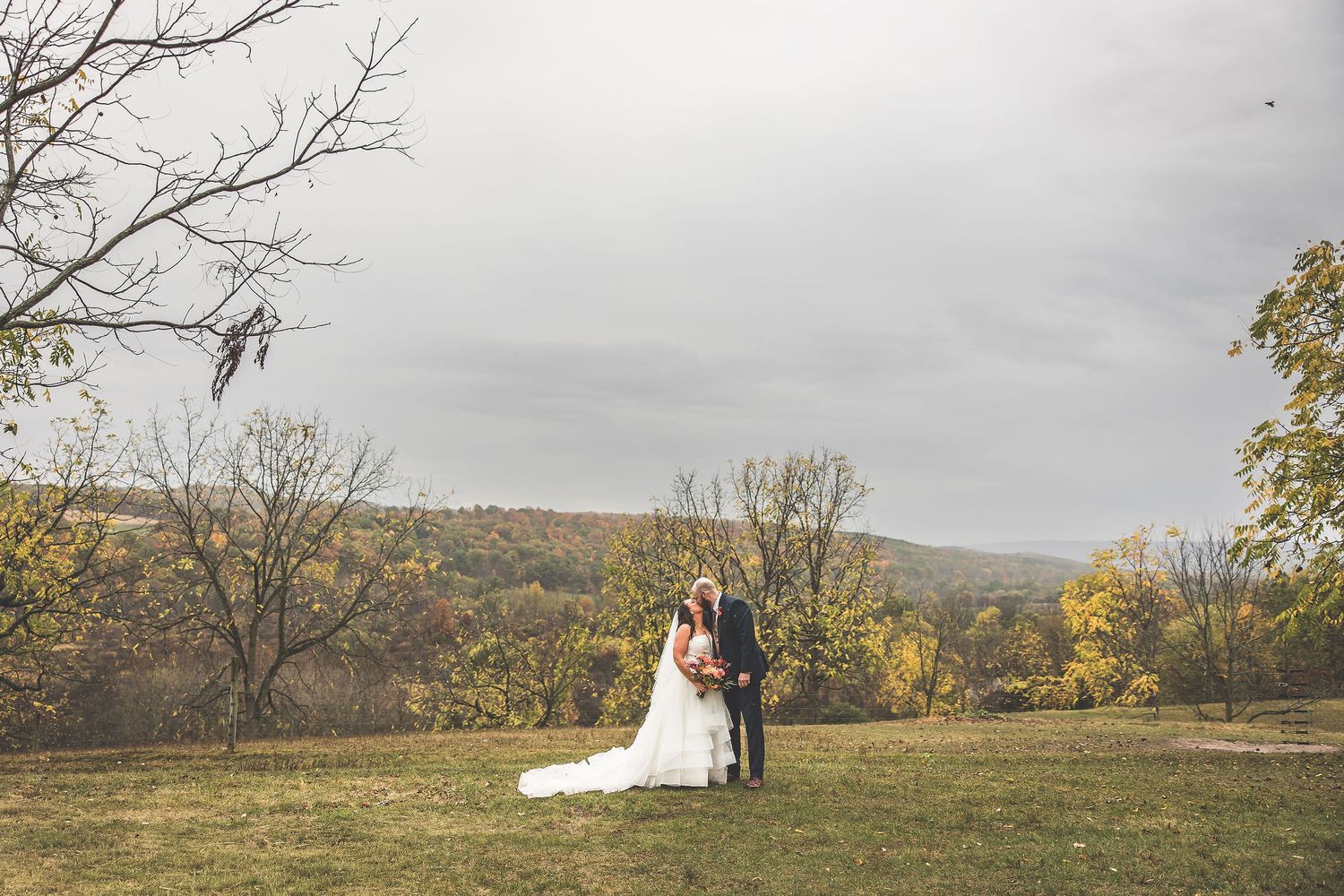A romantic wedding portrait showing a couple in the distance against rolling autumn hills.