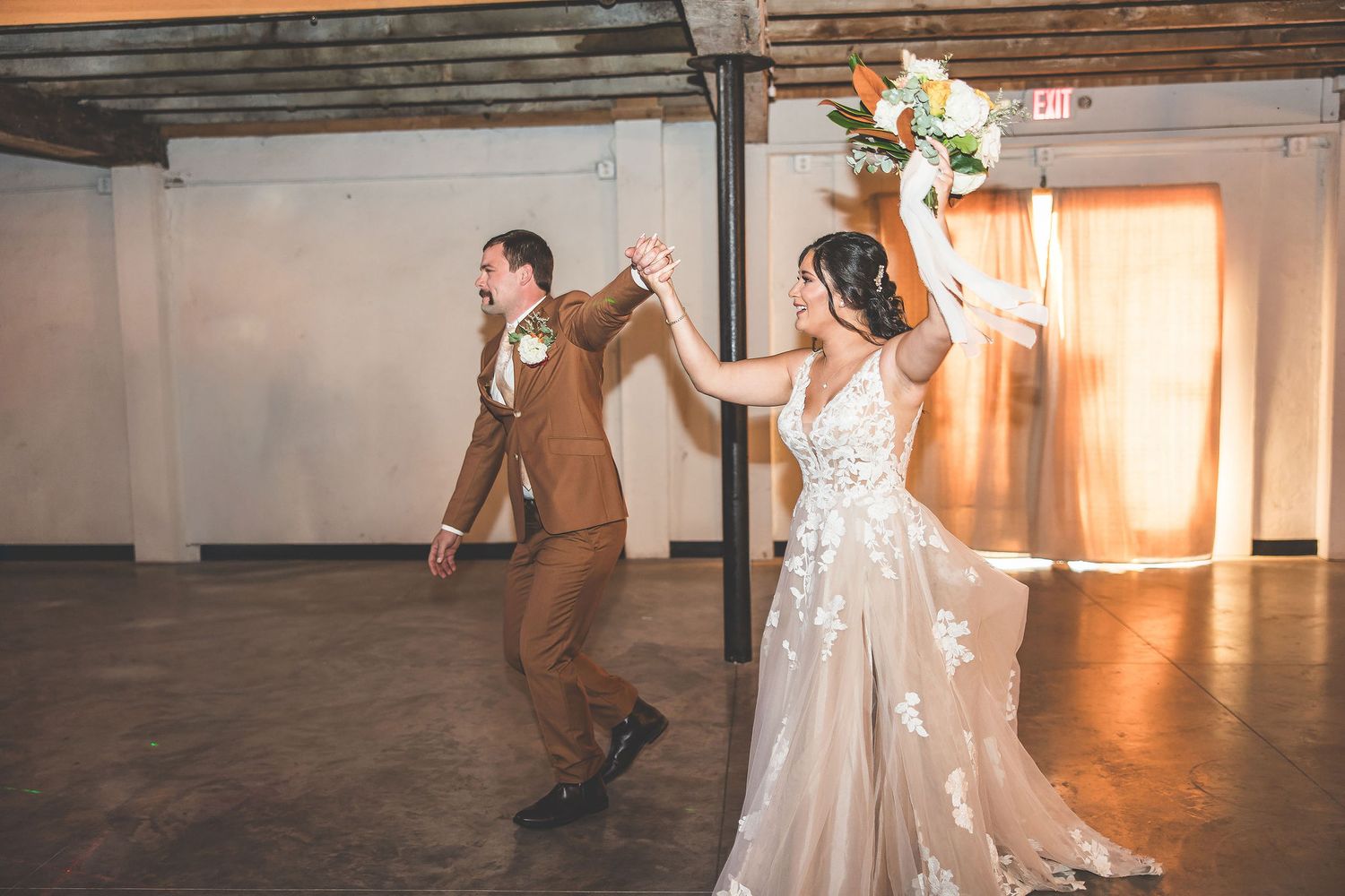 A couple performs an elegant dance move during their first dance at a rustic wedding reception venue.